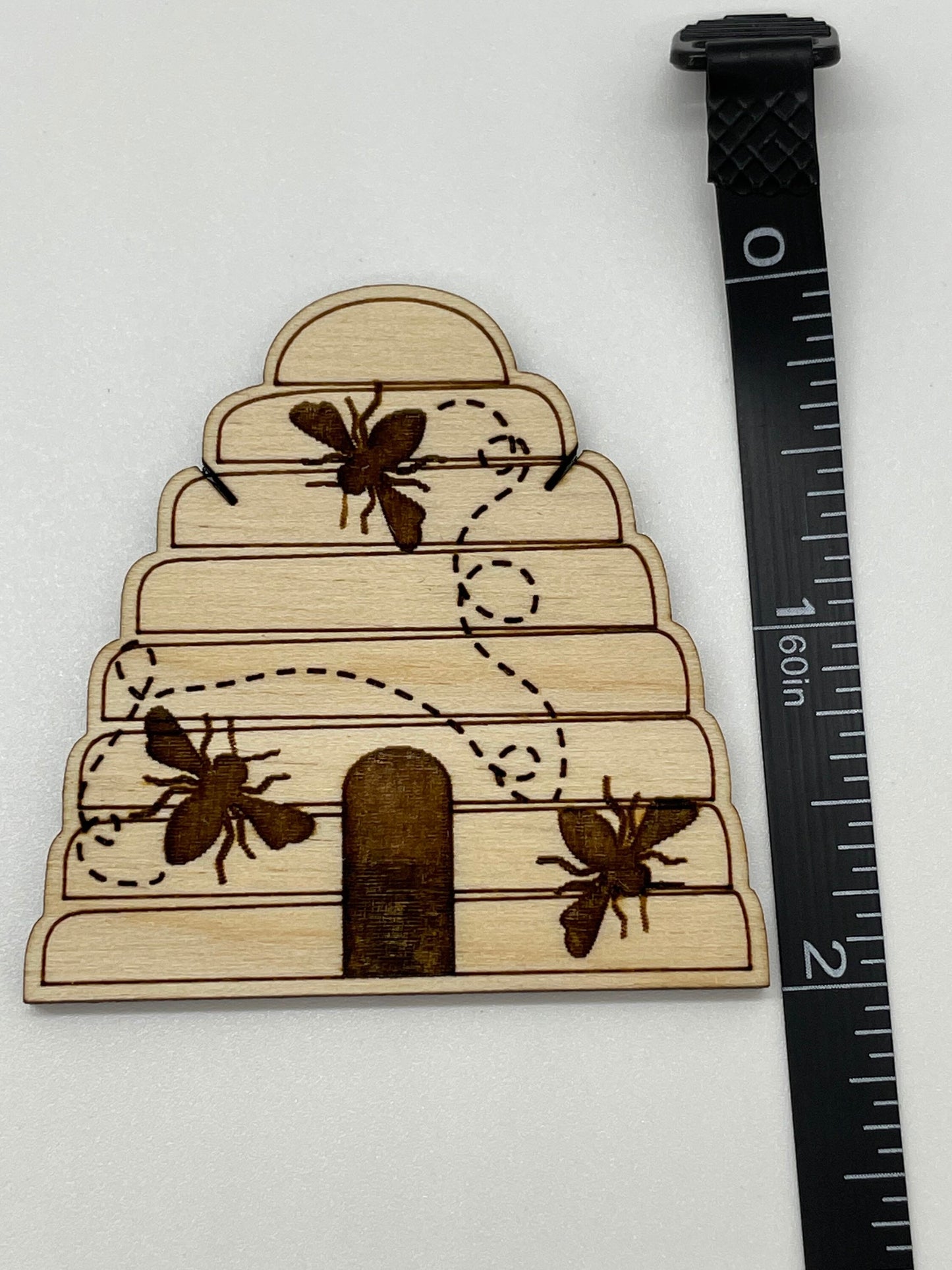 Wooden beehive-shaped ornament with bees and a ruler for scale on a white background