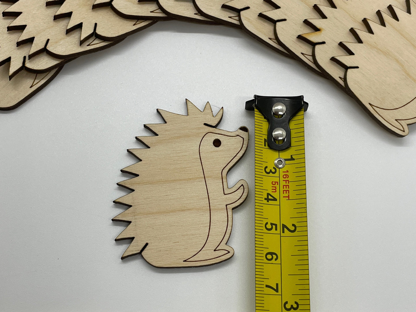 Wooden hedgehog bobbin with a measuring tape for scale on a white background
