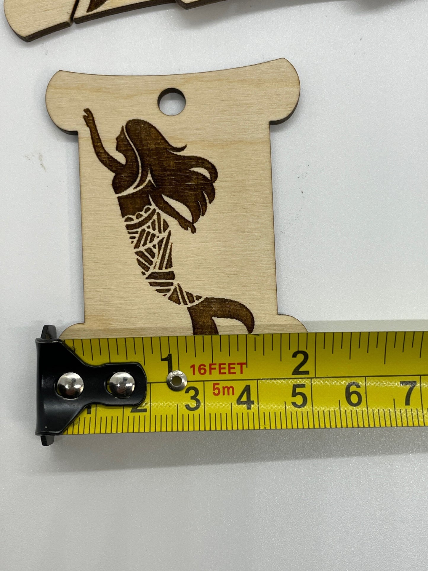 Wooden cutout of a stylized mermaid figure with a measuring tape for scale on a white background