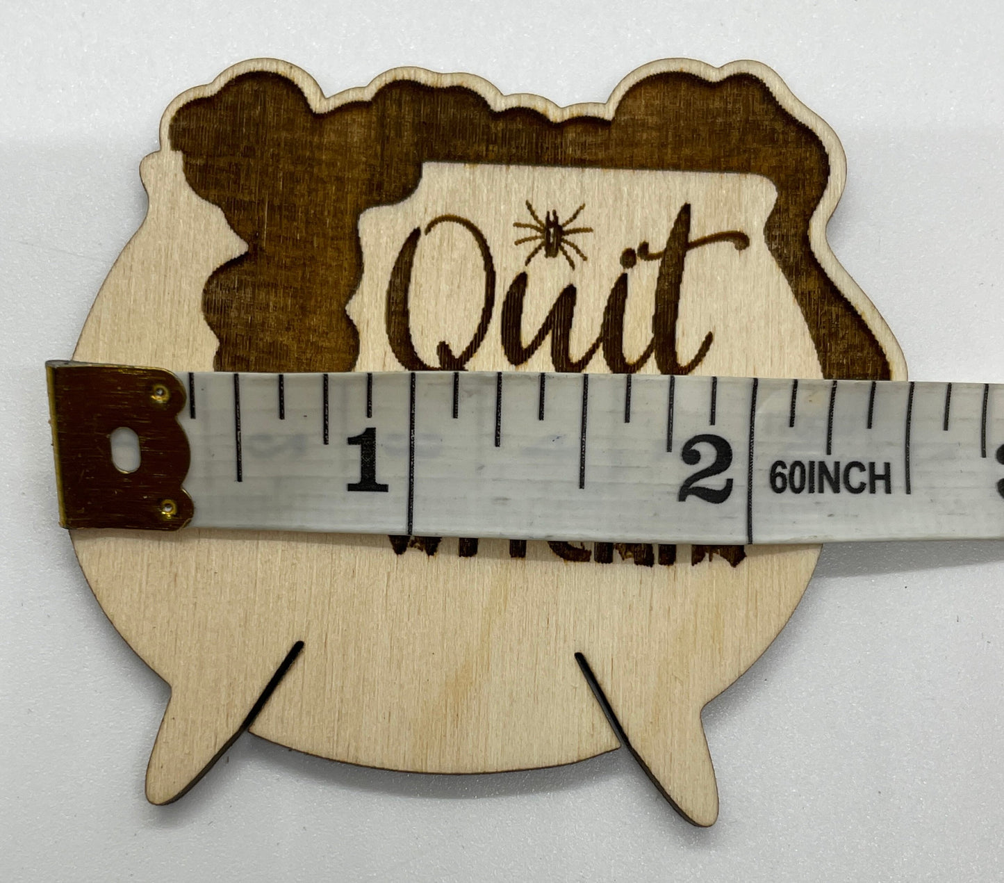 Wooden sign with 'Quit' and spider design, measured by a ruler on a white background