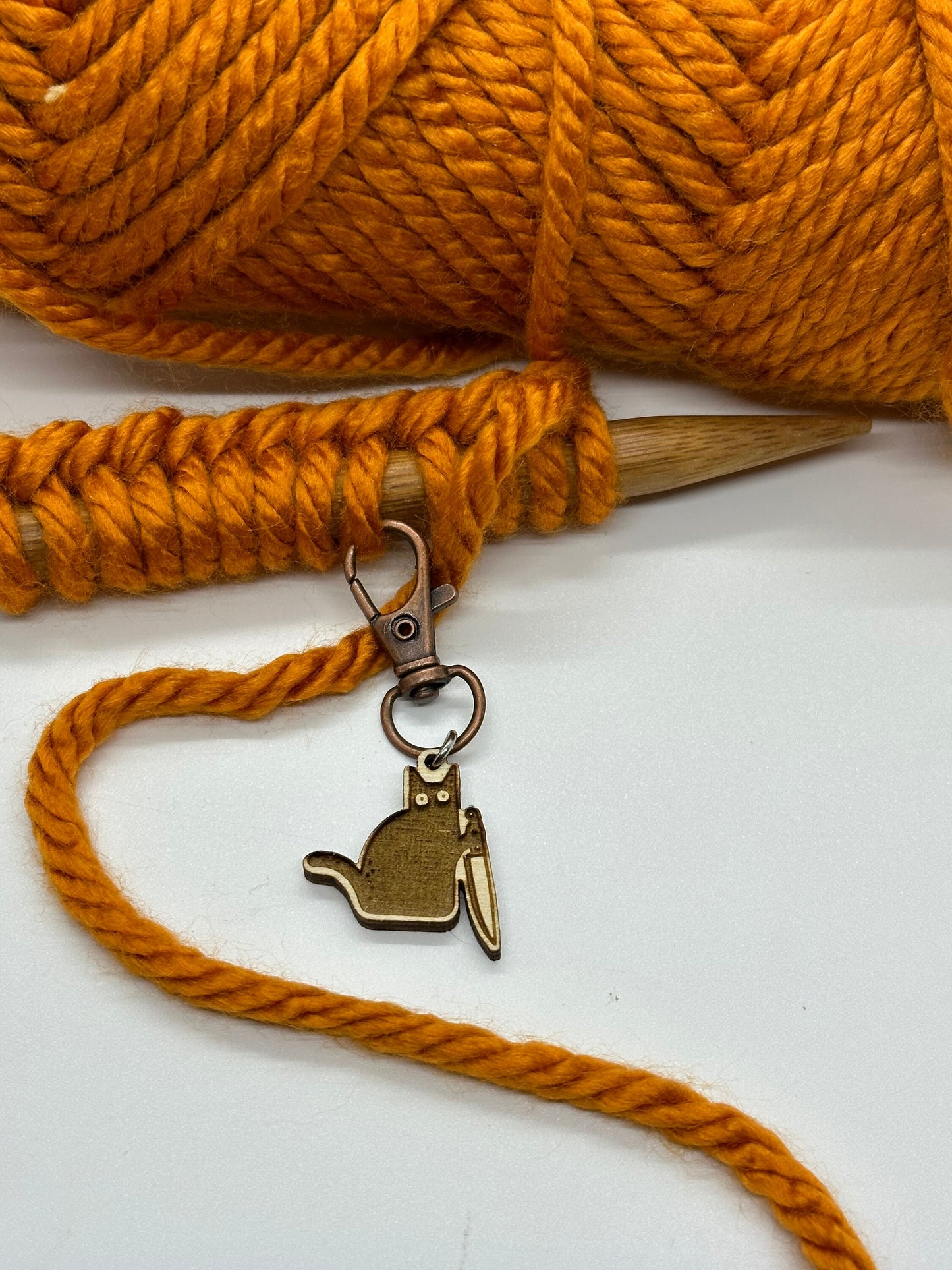 Knitting project with orange yarn and a gold cat-shaped keychain on a white background