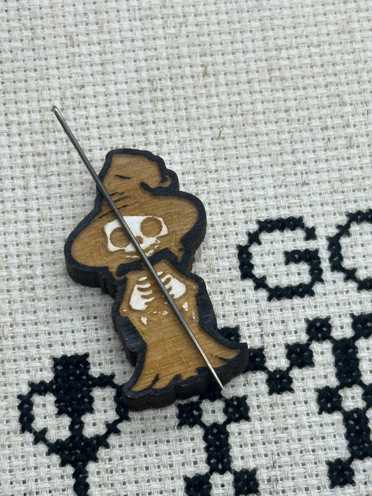 Cross-stitch pattern with a skeleton witch holding a bone on fabric.