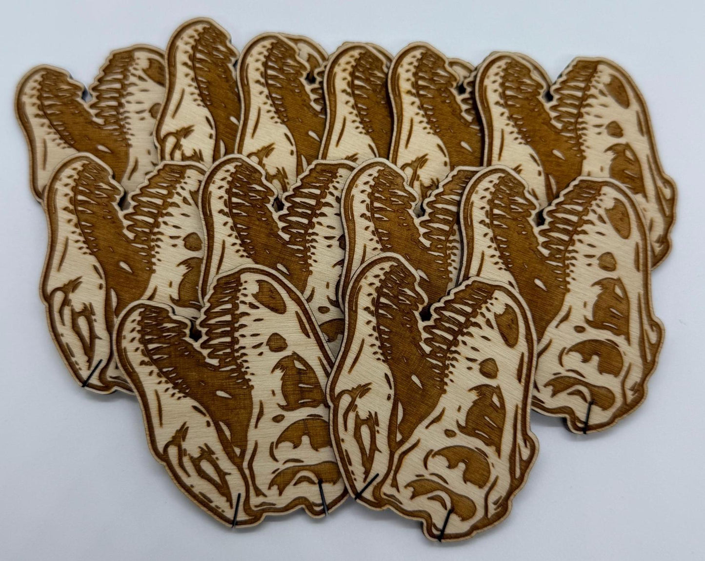 Set of 12 laser engraved dinosaur skull wooden bobbins on white background, detailed T-rex skull design on birch