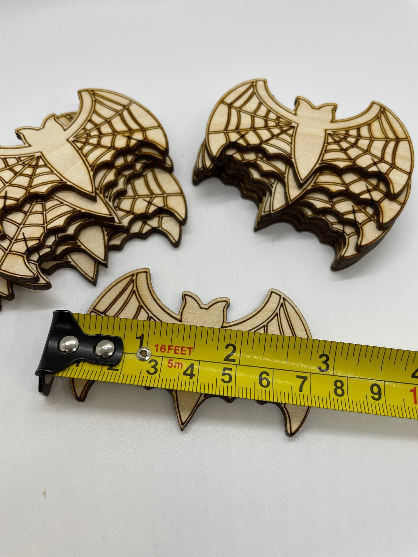 Wooden bat-shaped cutouts with spider web design on a white background, measured by a tape measure.
