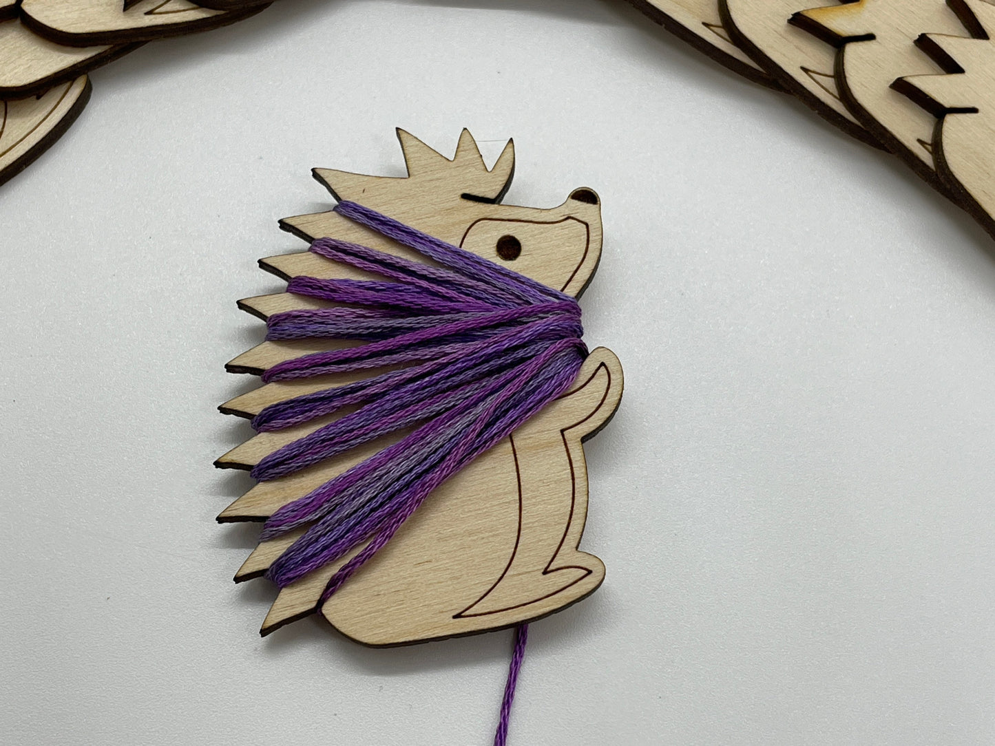 Wooden hedgehog bobbin with purple yarn on a white background