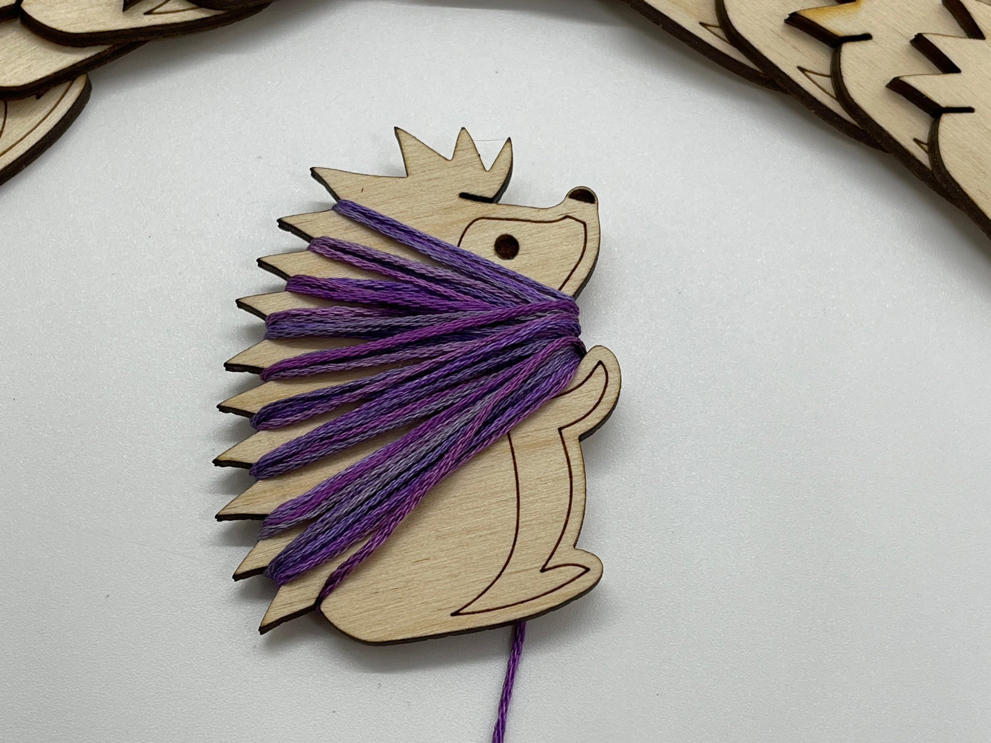 Wooden hedgehog bobbin with purple yarn on a white background