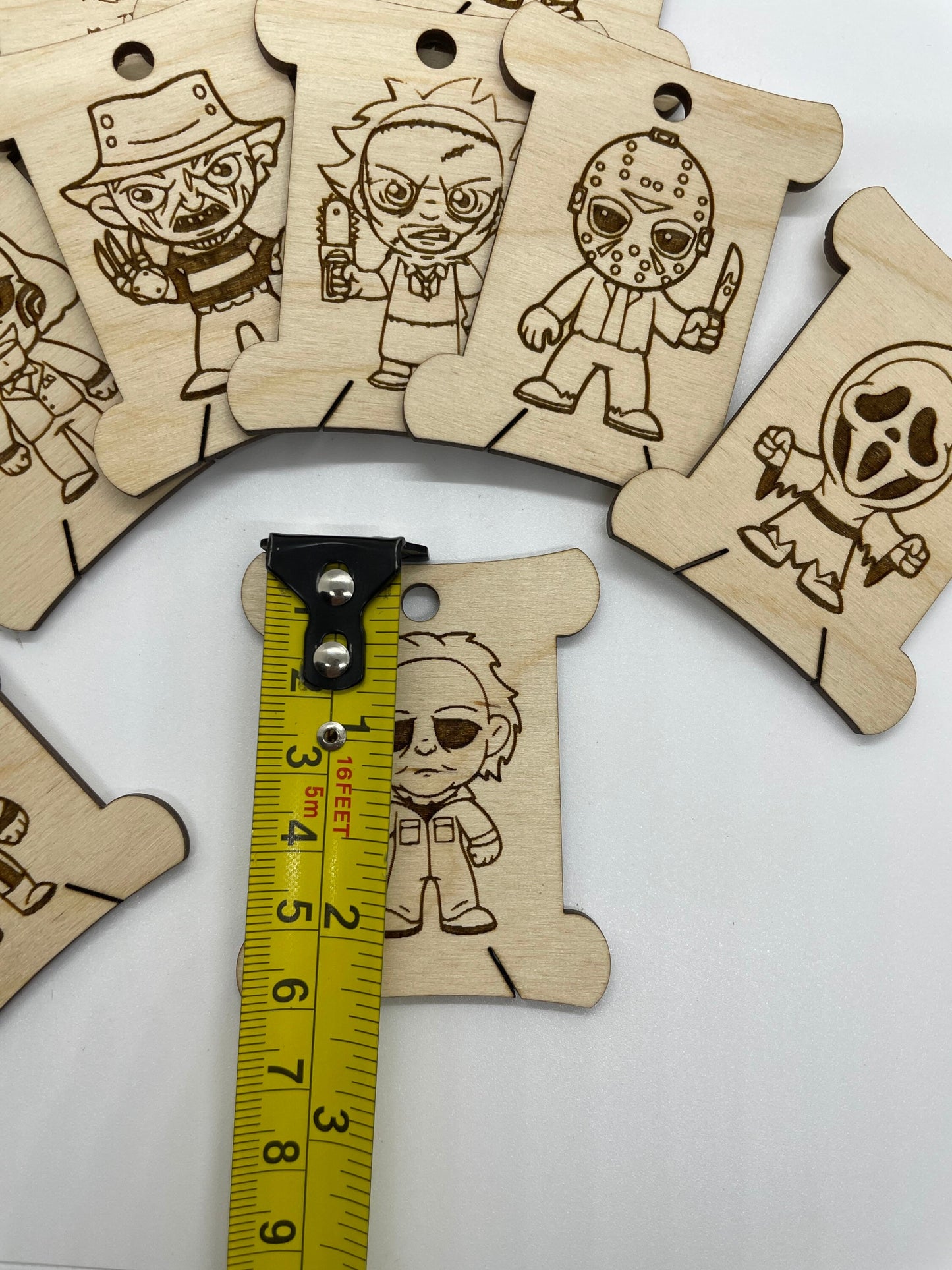 Wooden bobbins with character designs and a measuring tape for scale on a white background