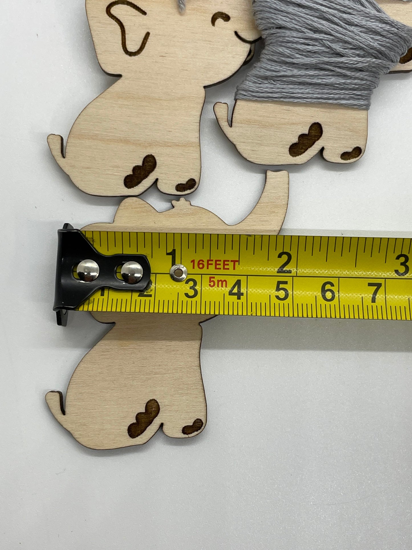 Wooden elephant cutout with a spool of gray thread, measured against a yellow ruler on a white background.