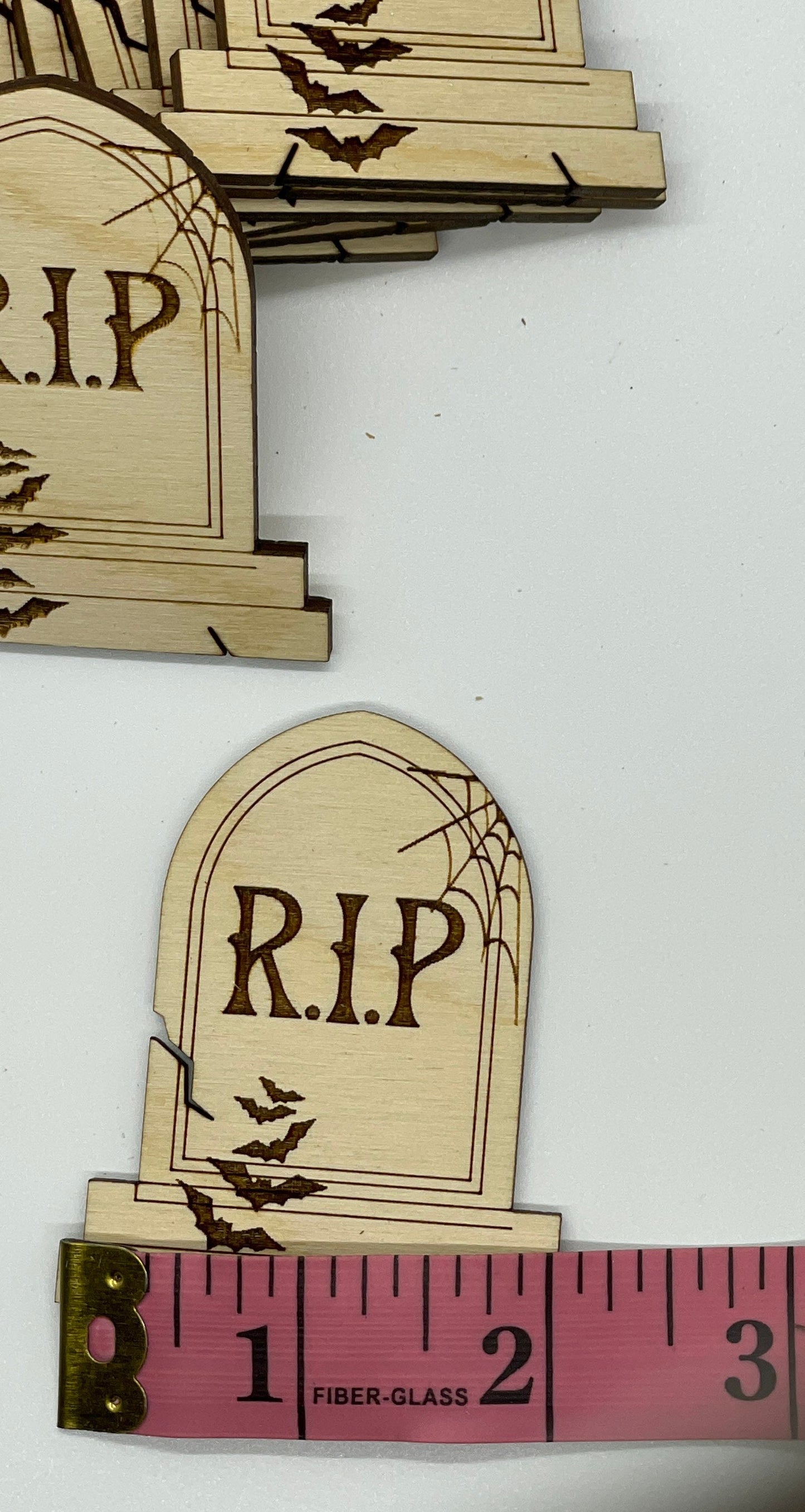 Wooden tombstone cutouts with 'R.I.P.' text on a white background, one with a measuring tape for scale.