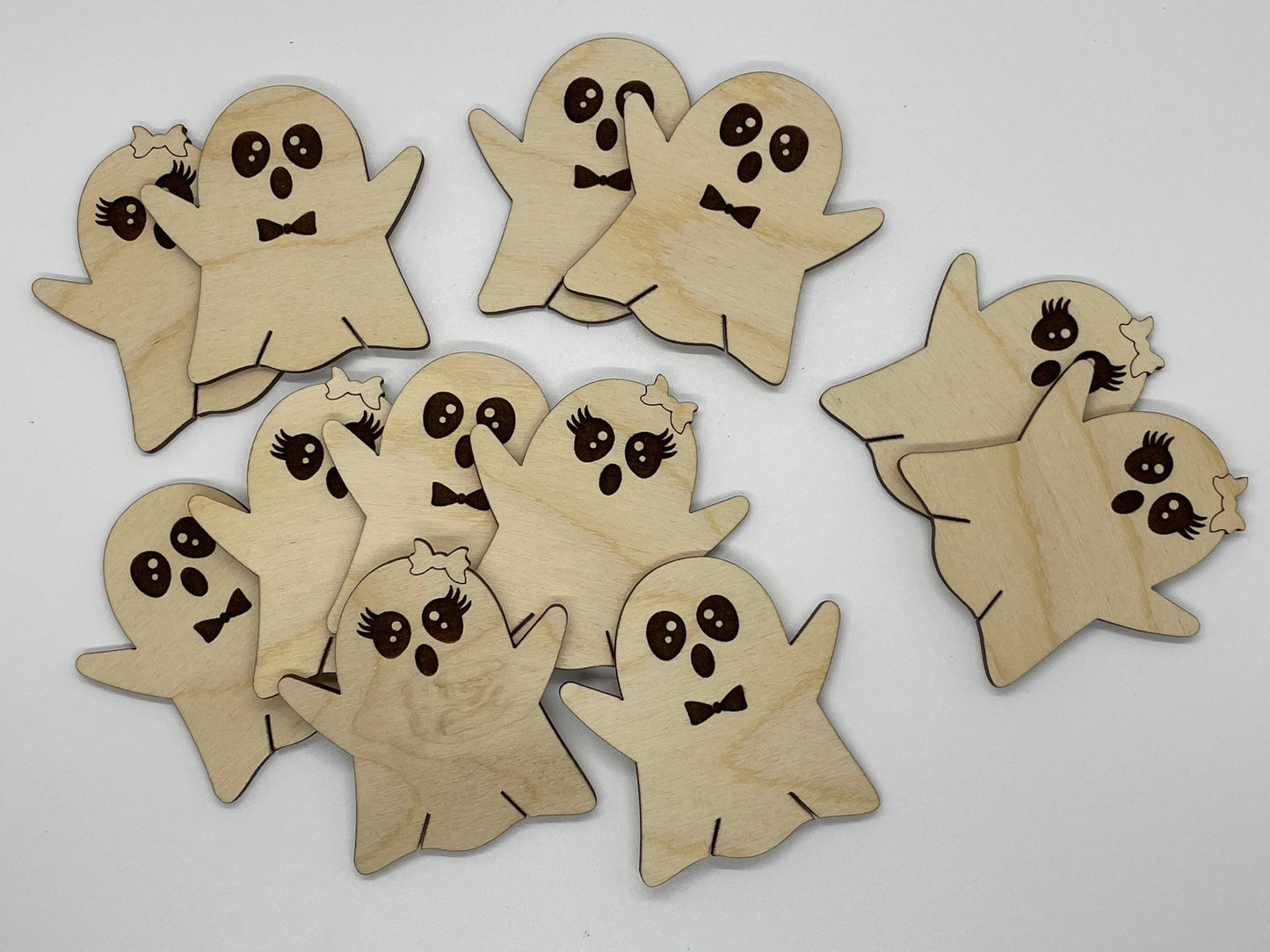 Wooden ghost cutouts with facial expressions on a light gray background