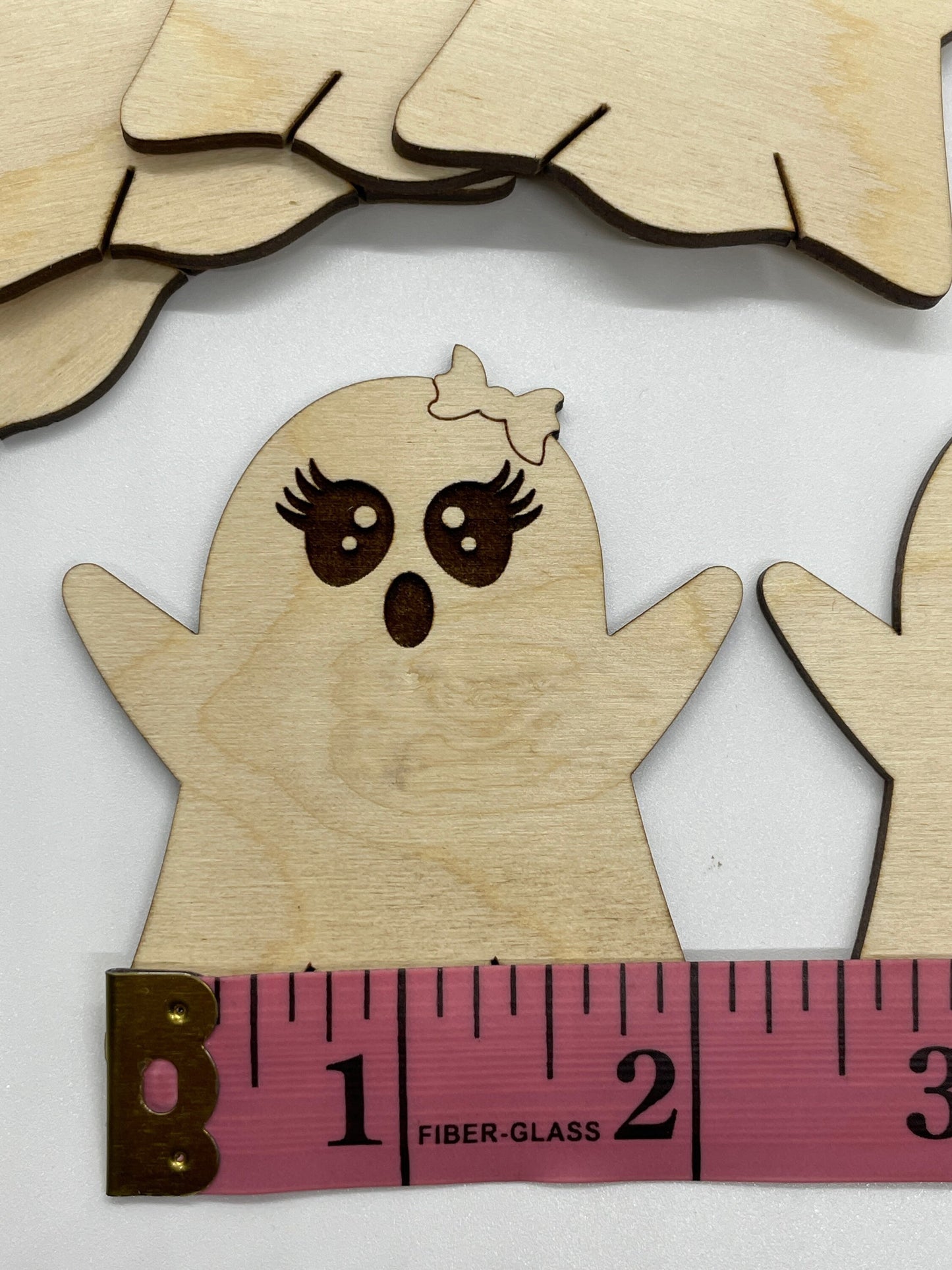 Wooden ghost cutout with a measuring tape for scale on a white background