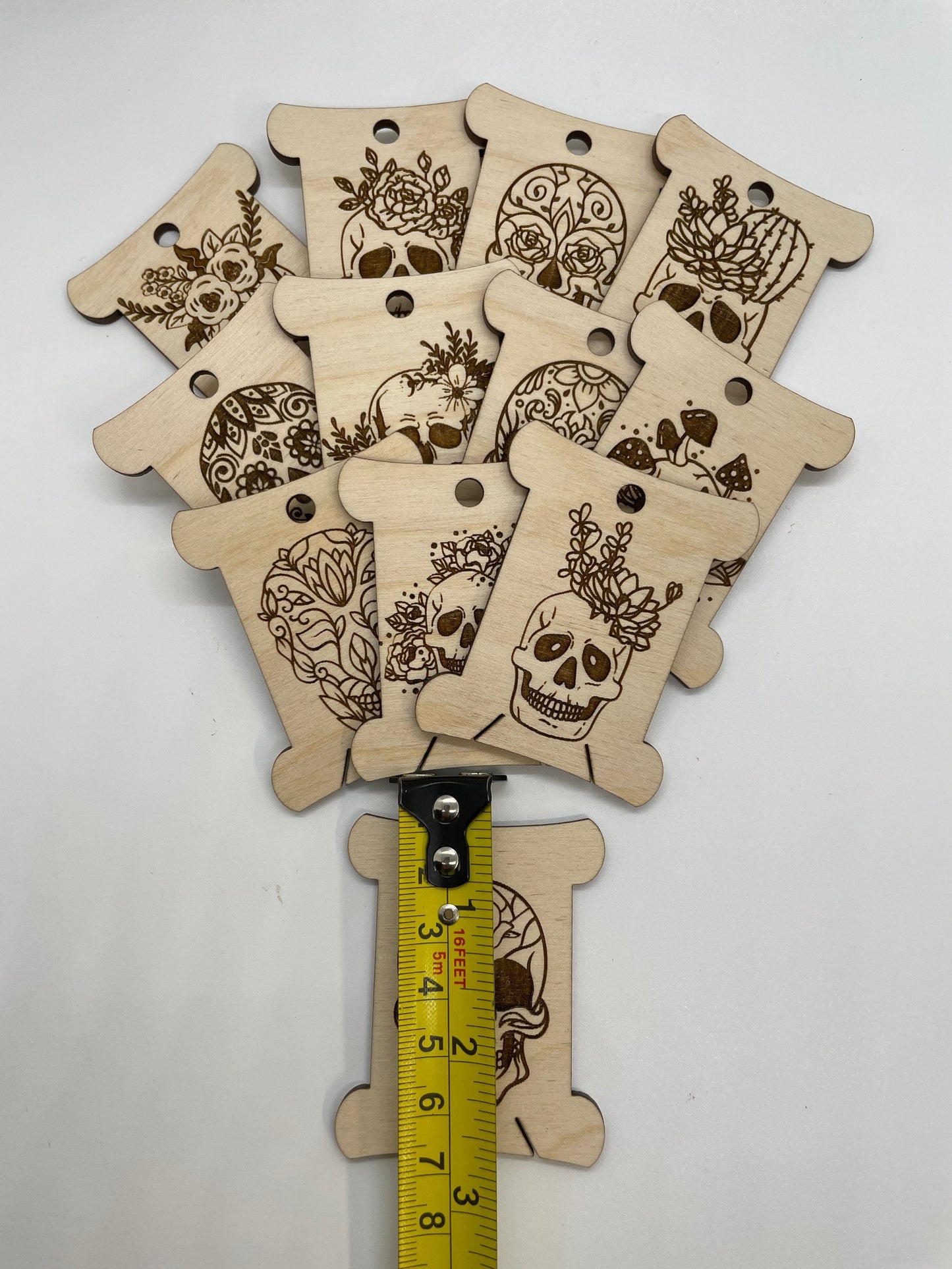 Wooden tags with skull designs and a measuring tape for scale on a white background