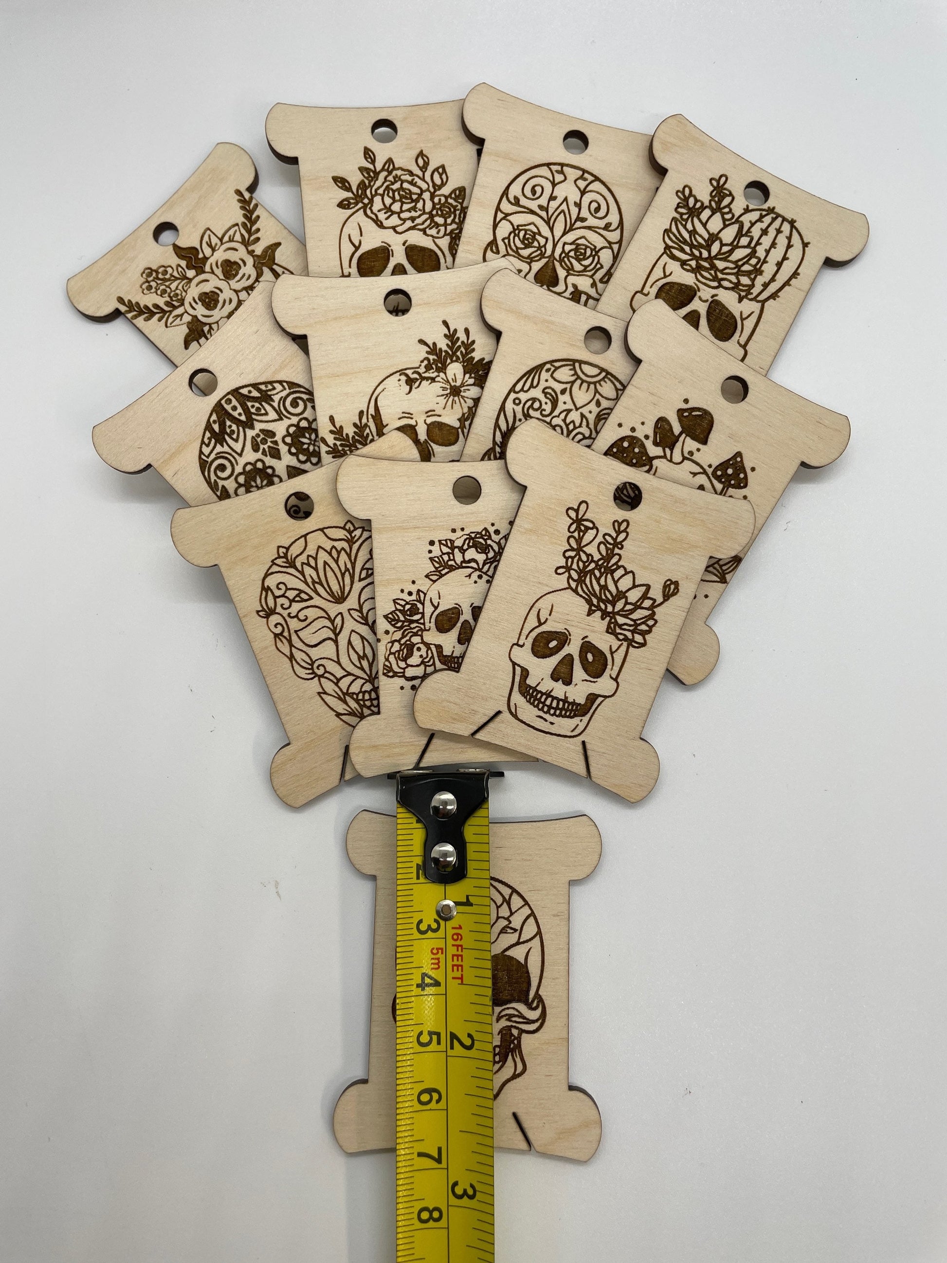 Wooden tags with skull designs and a measuring tape for scale on a white background
