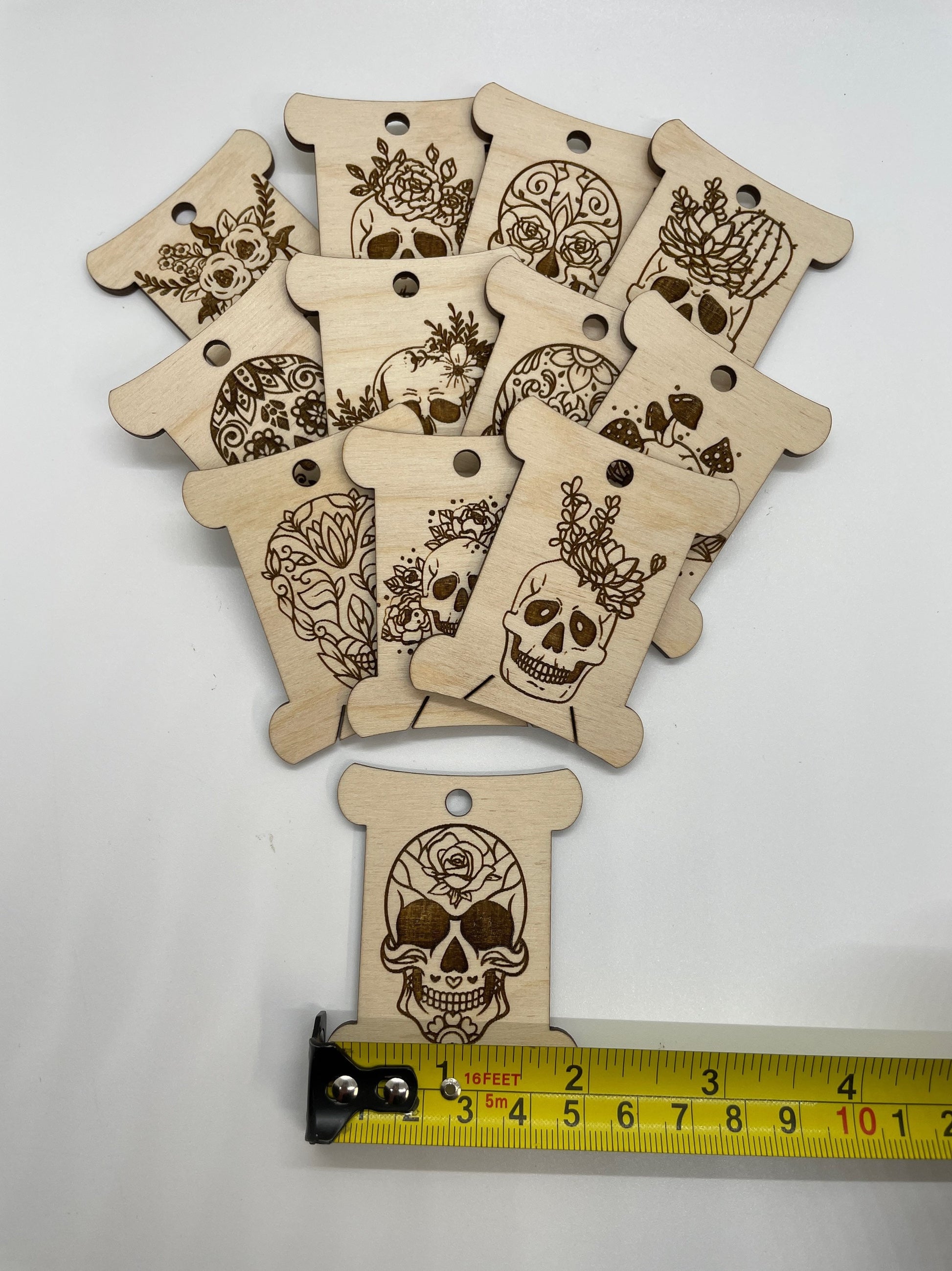 Wooden tags with skull designs on a white background, measured with a ruler.