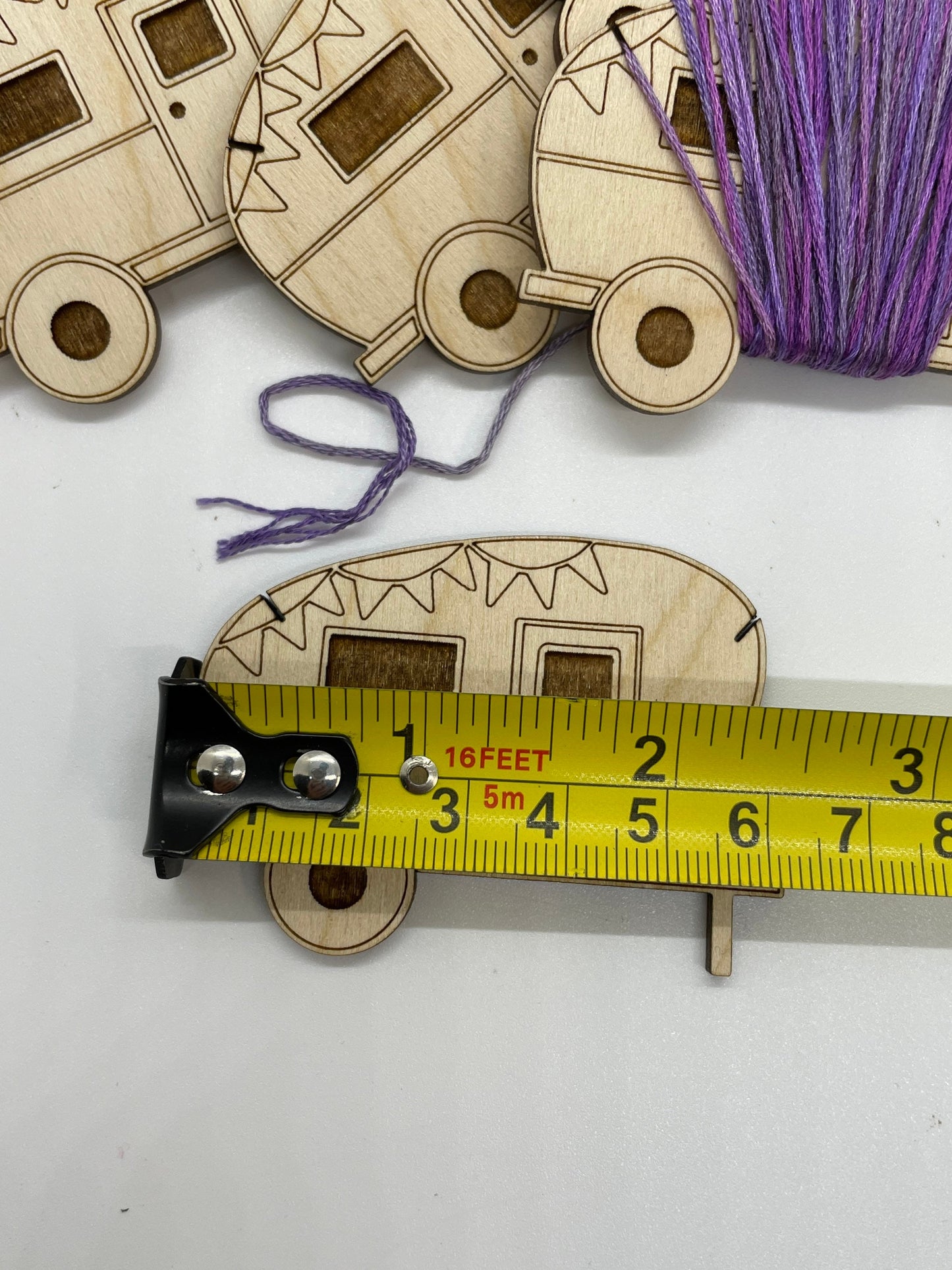 Wooden camper with purple thread and a measuring tape on a white background