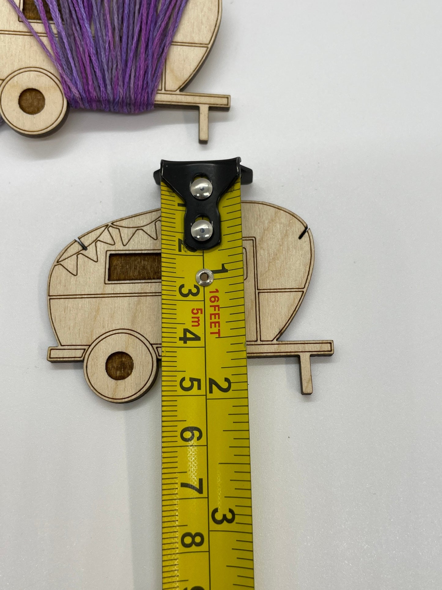 Wooden caravan-shaped cutout with a measuring tape for scale on a white background