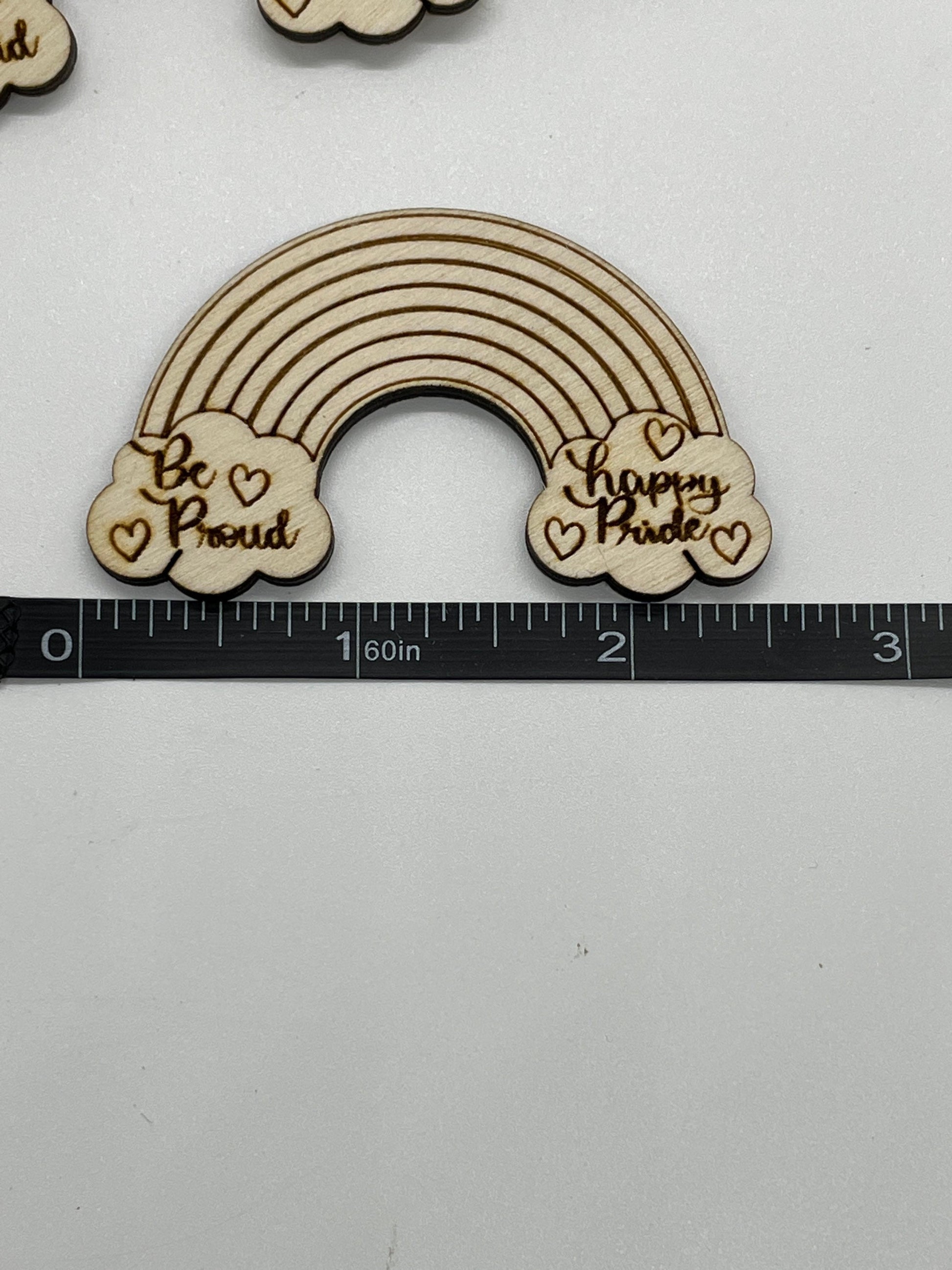 Wooden rainbow decoration with 'Be Proud' and 'Happy Pride' text on a white background with a ruler for scale.