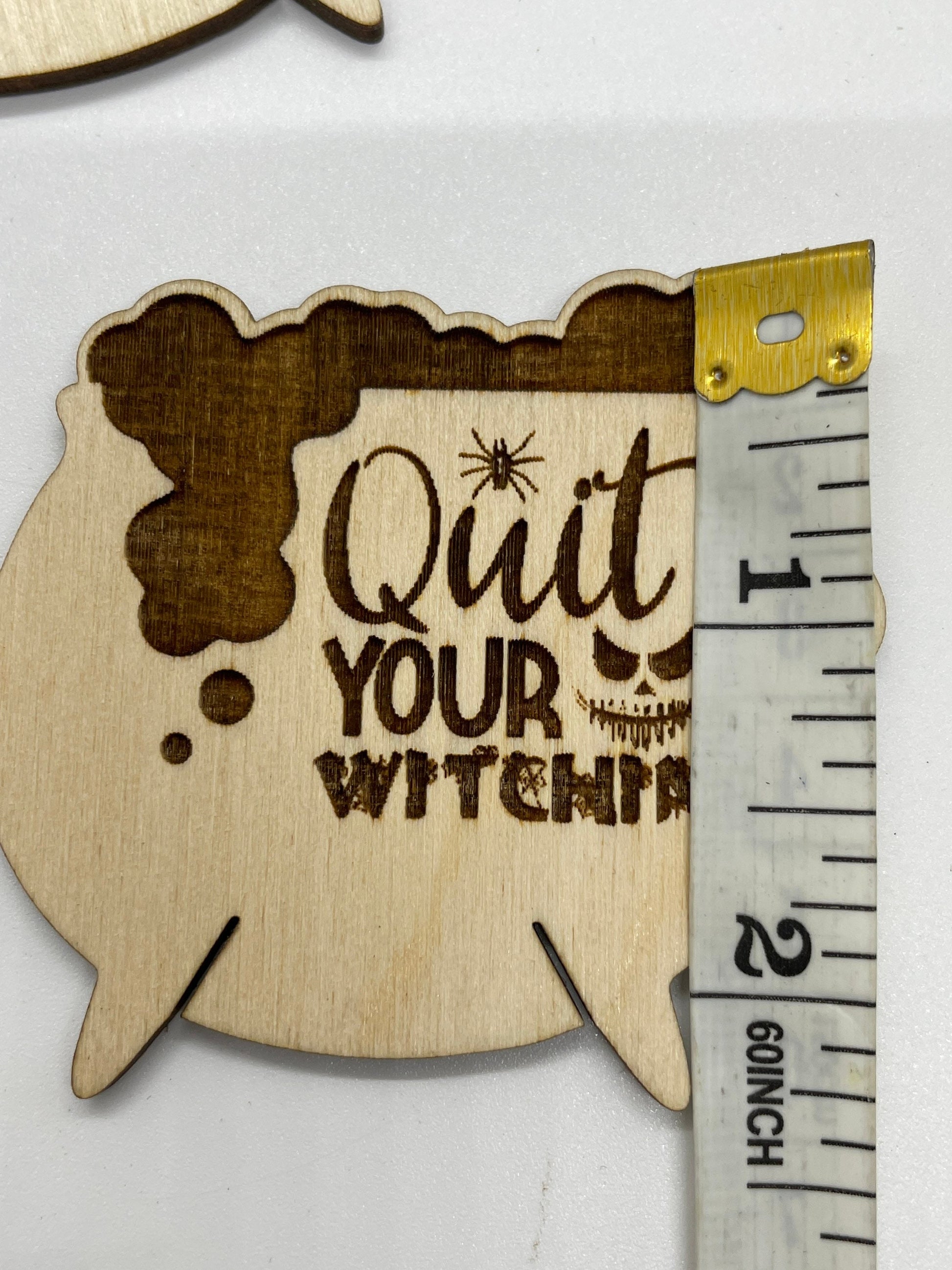 Wooden cutout with 'Quit Your Witchery' text next to a ruler for size reference