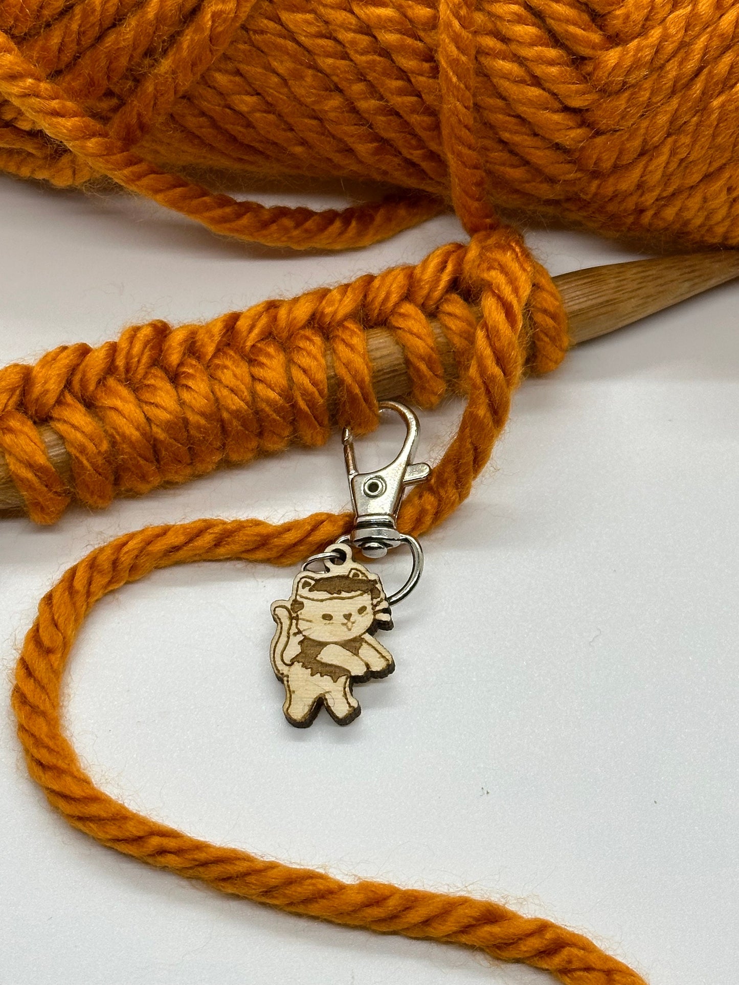 Orange yarn with a wooden knitting needle and a cat-shaped keychain on a white background
