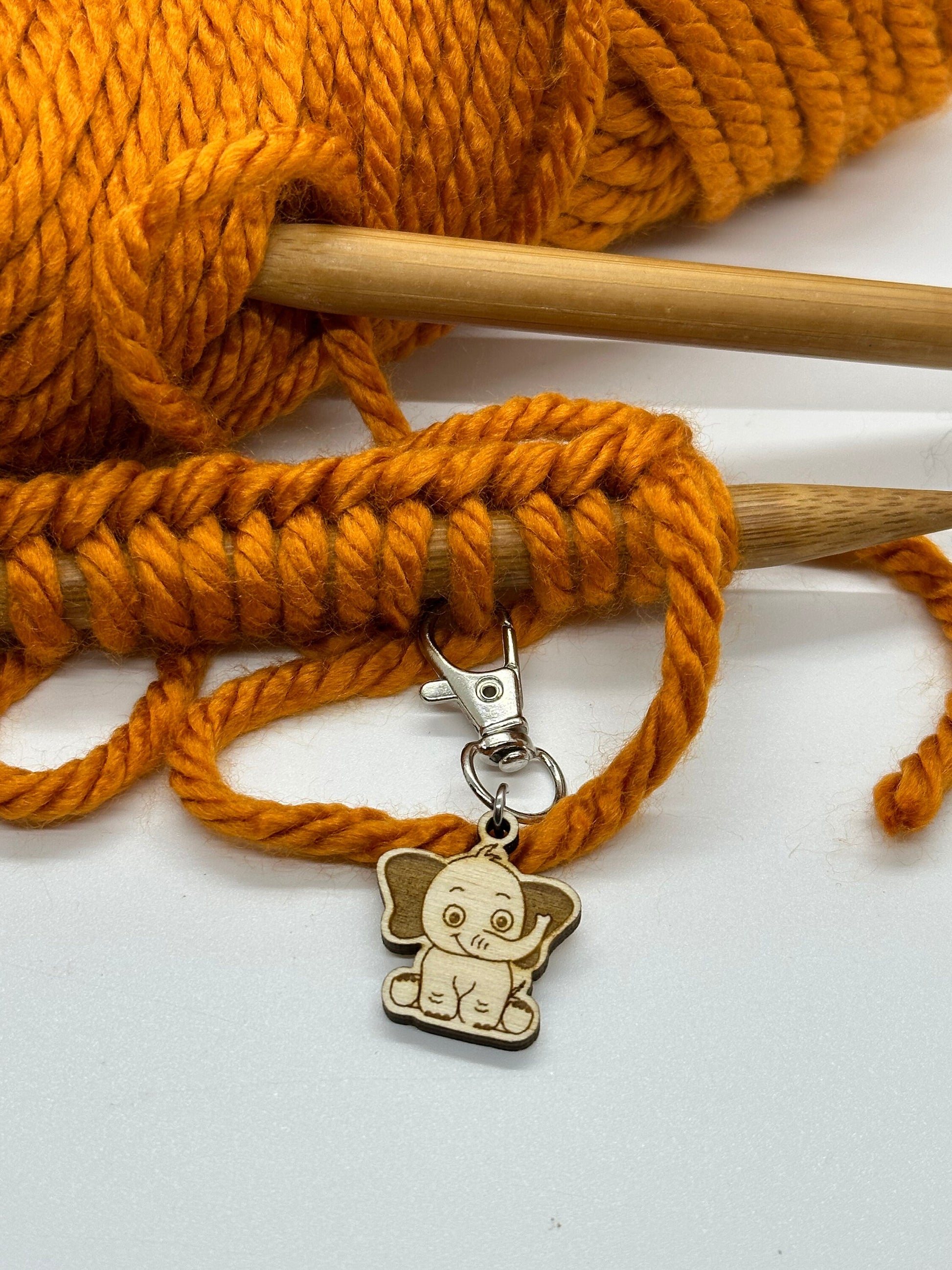 Orange yarn with knitting needles and a wooden elephant charm on a white background