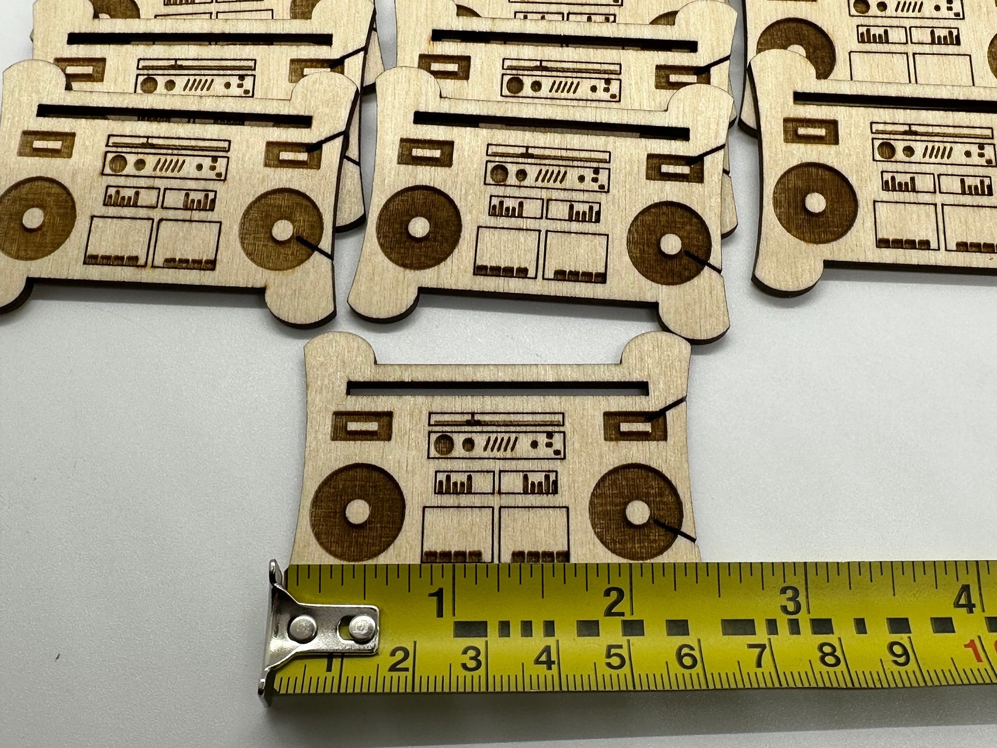 Wooden cutouts of boomboxes with a tape measure for scale on a white background