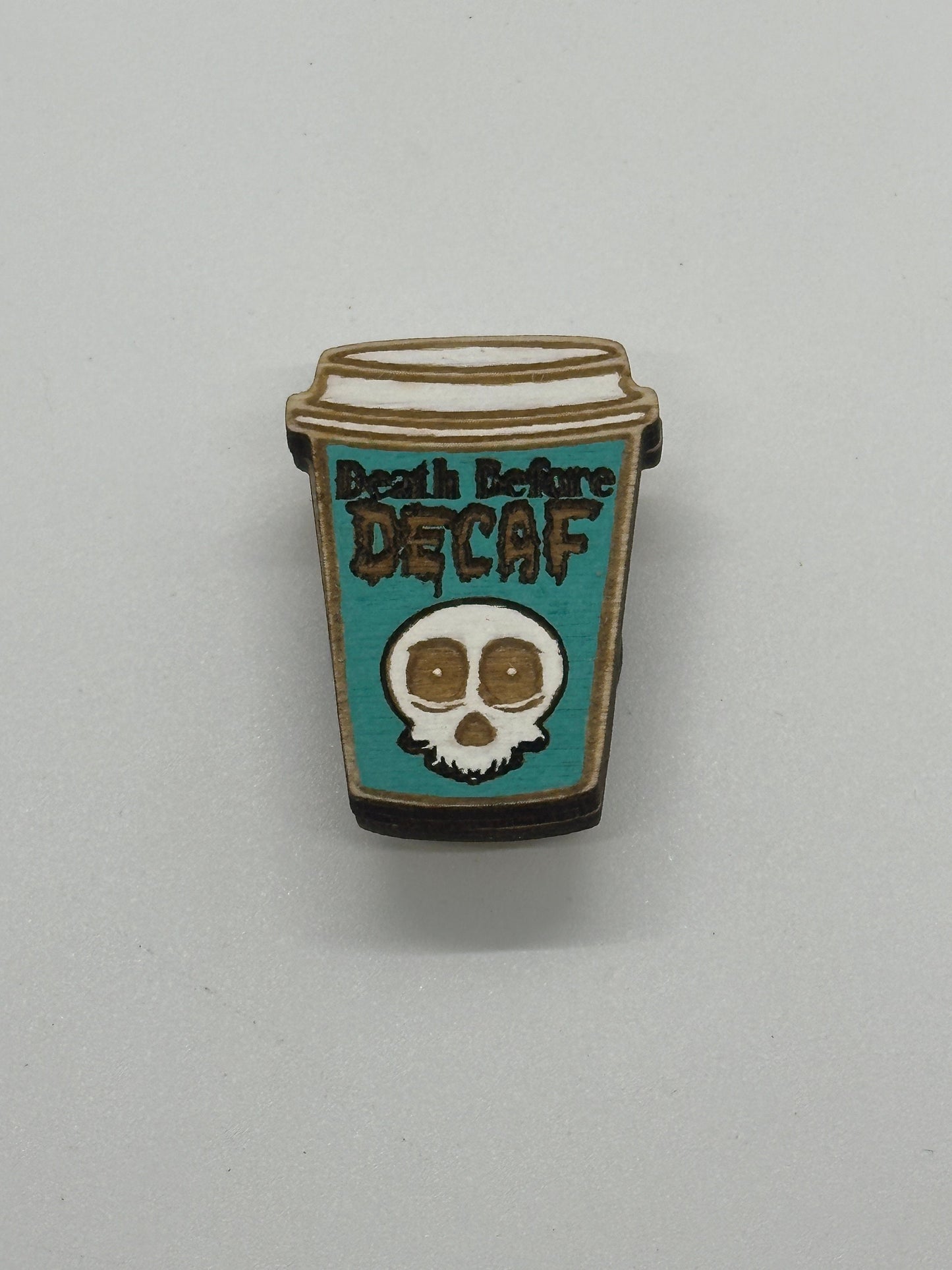 Pin shaped like a coffee cup with a skull design and 'Death Before Decaf' text on a gray background.