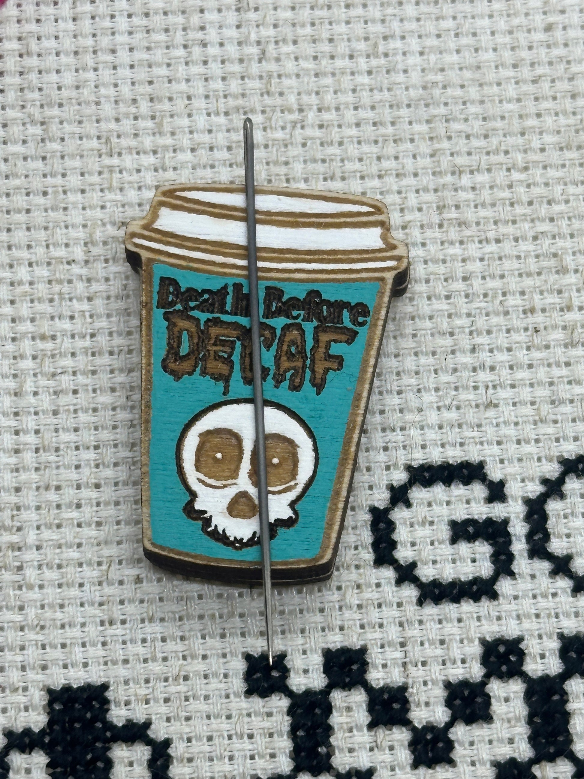 pin shaped like a coffee cup with 'Death Before Decaf' text on a textured fabric background.