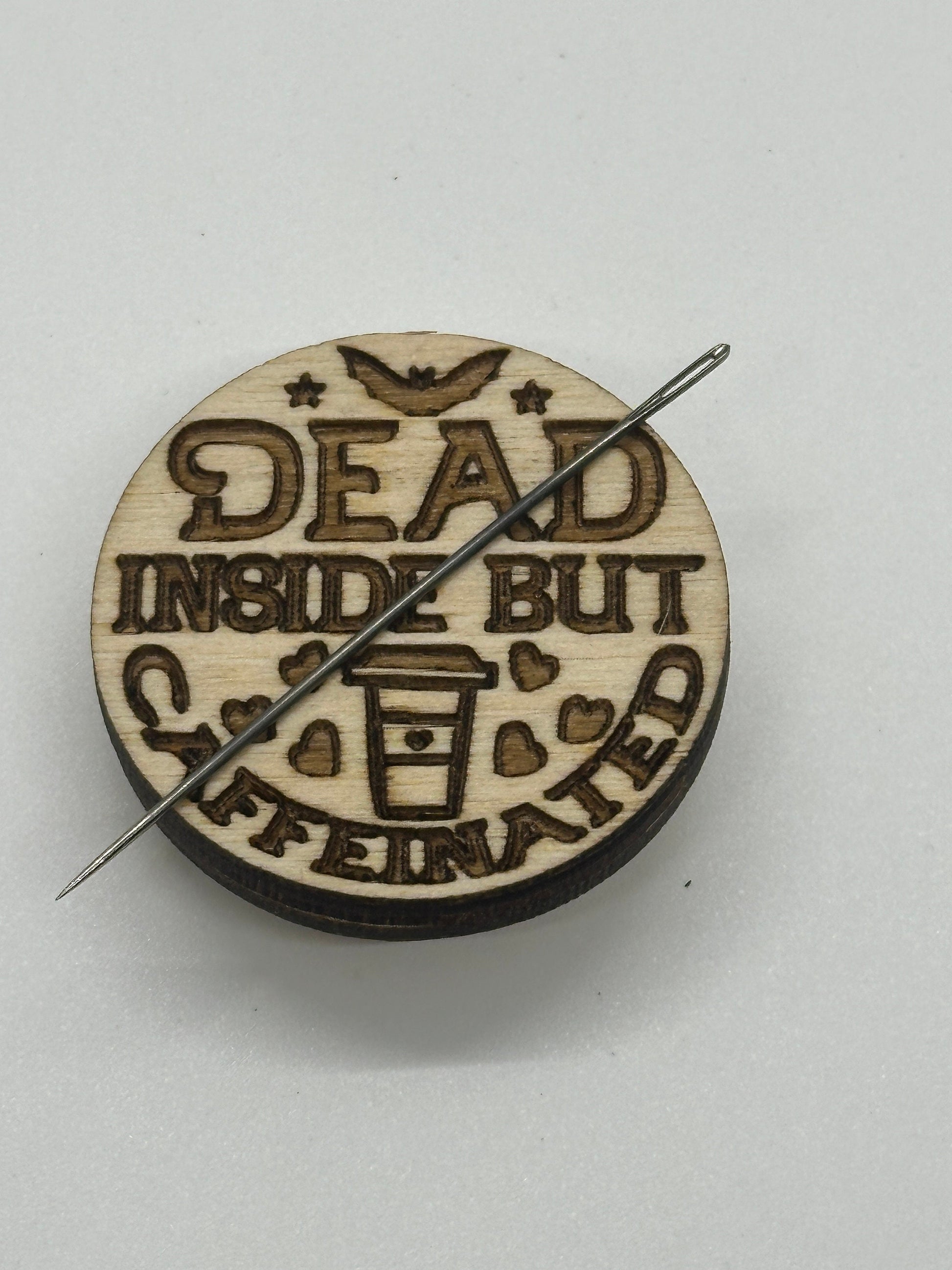 Wooden button with laser engraving and a needle on a light gray background