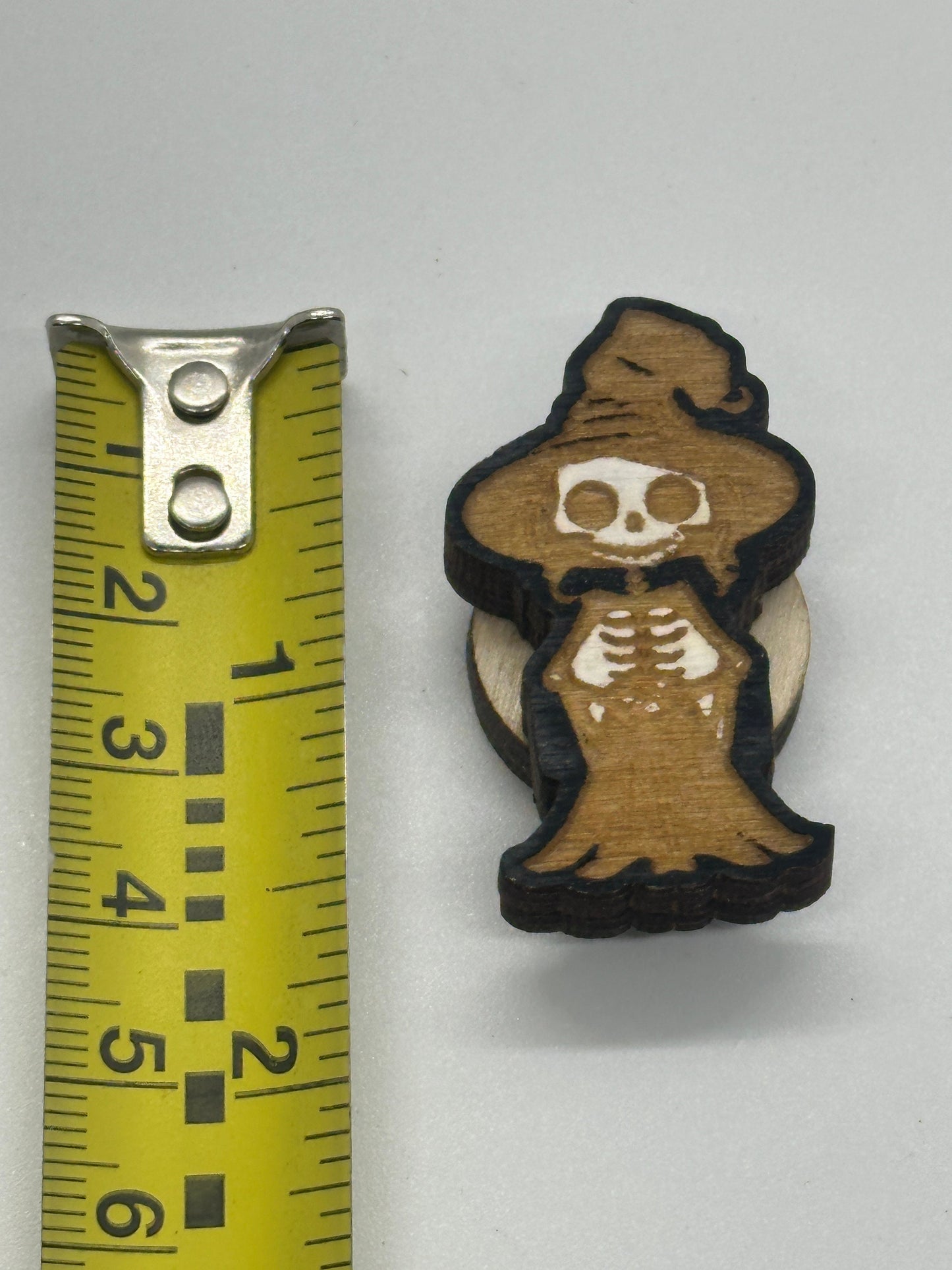 Small skeleton figurine with a hat next to a measuring tape on a white background