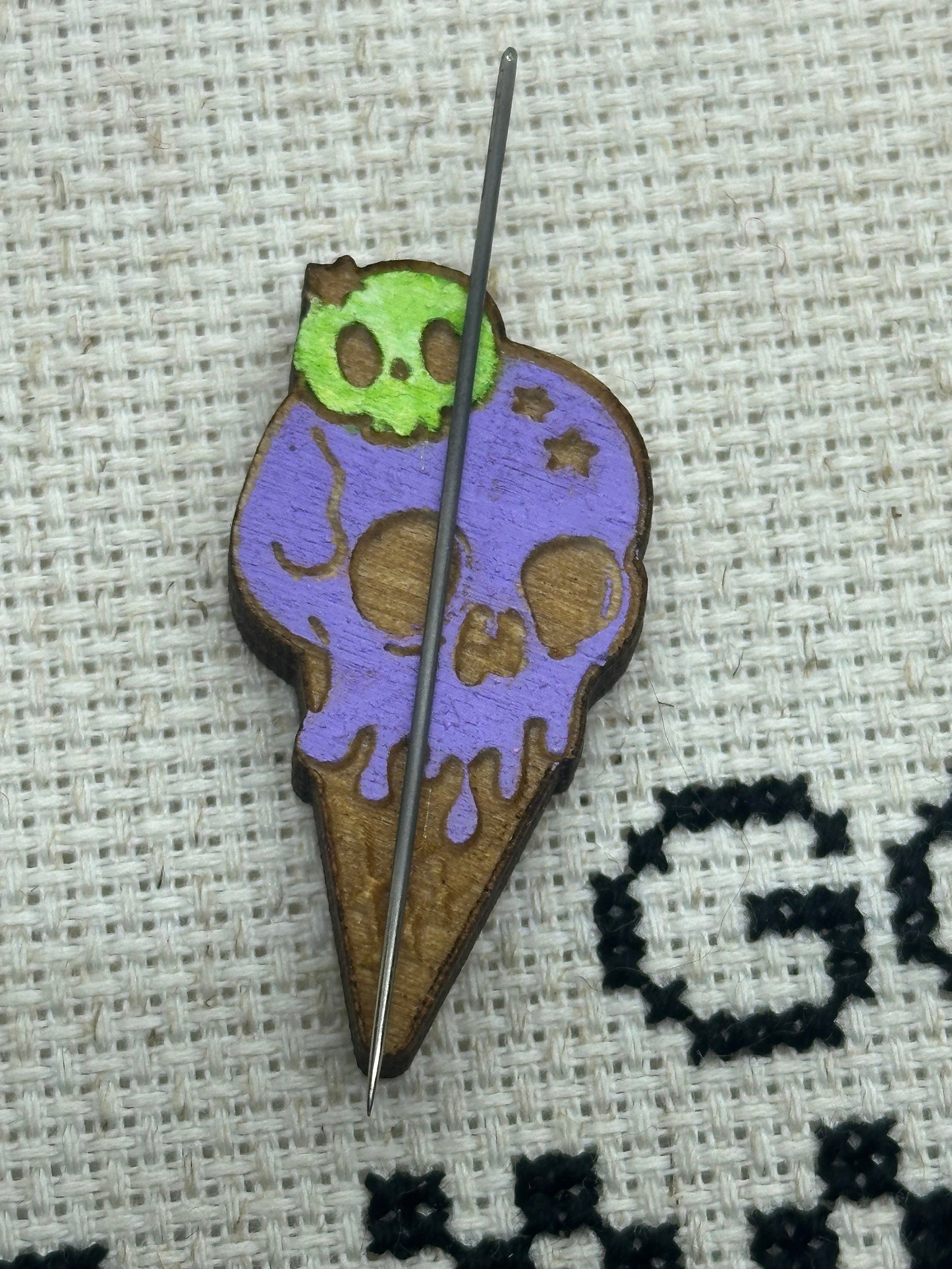 Colorful ice cream cone-shaped pin with skull design on a textured fabric background