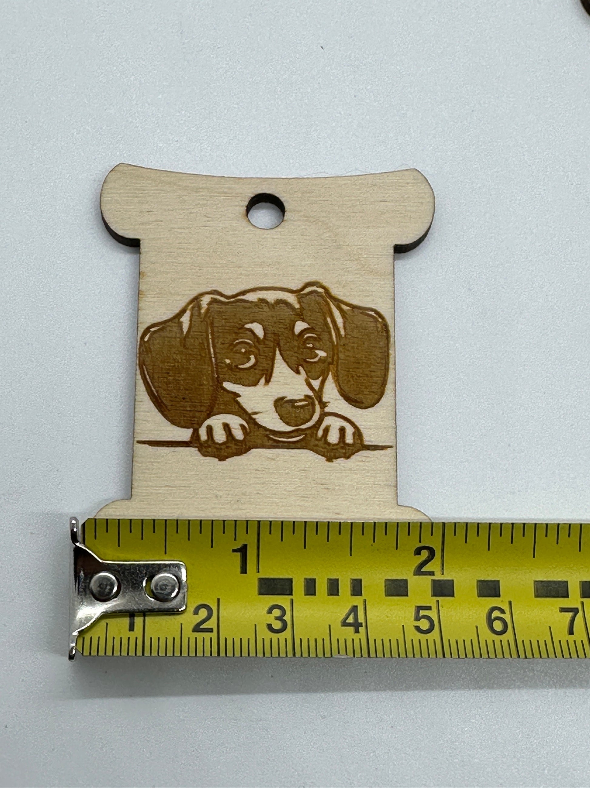Wooden bobbin with a dog illustration and a measuring tape for scale on a white background