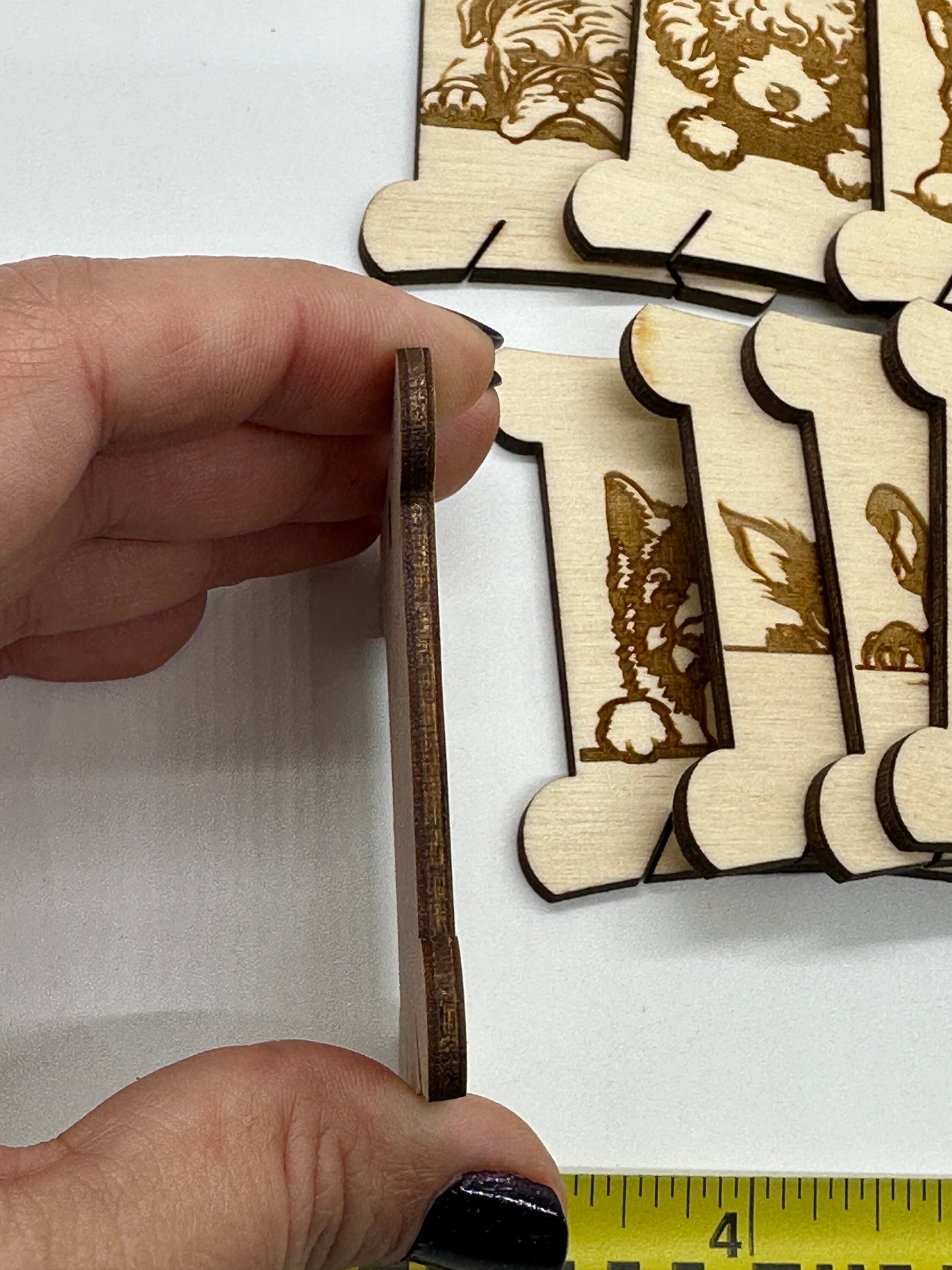 Wooden bobbin with dog designs  held by a hand with a ruler for scale.
