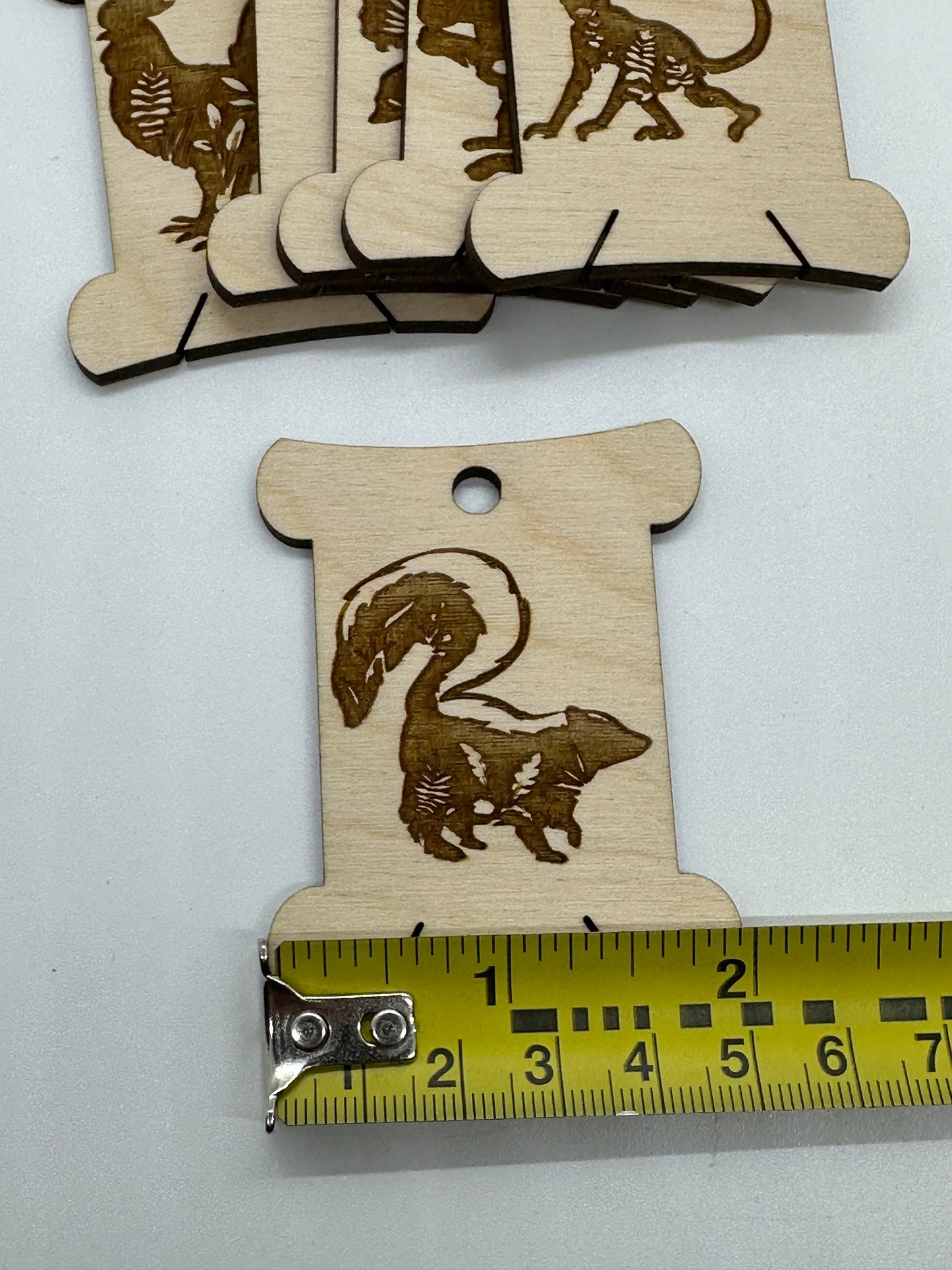 Wooden cutouts with engraved animal designs on a white background, one with a measuring tape for scale.