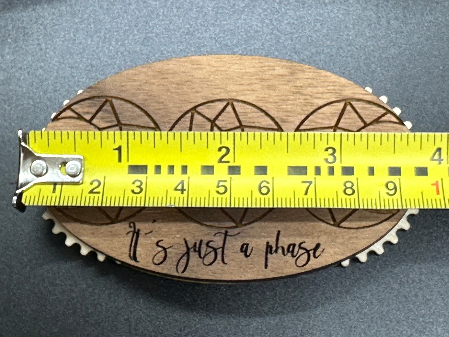 Wooden counter with geometric design and 'It's just a phase' text, measured by a yellow tape measure on a gray background.