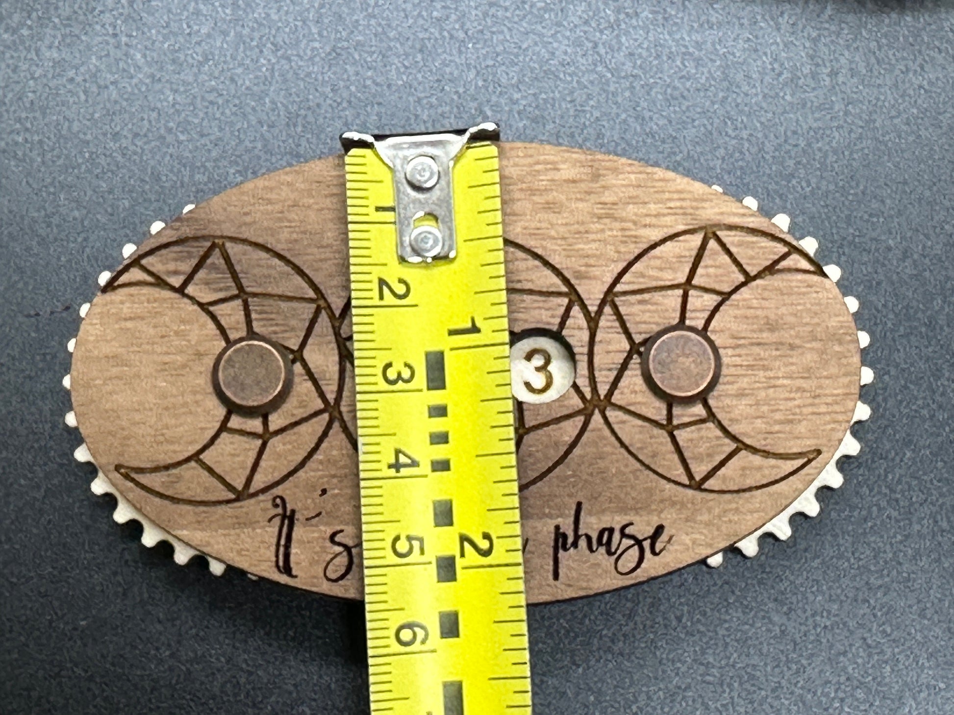Wooden gear-like object with engraved design and measurement tape on a gray background