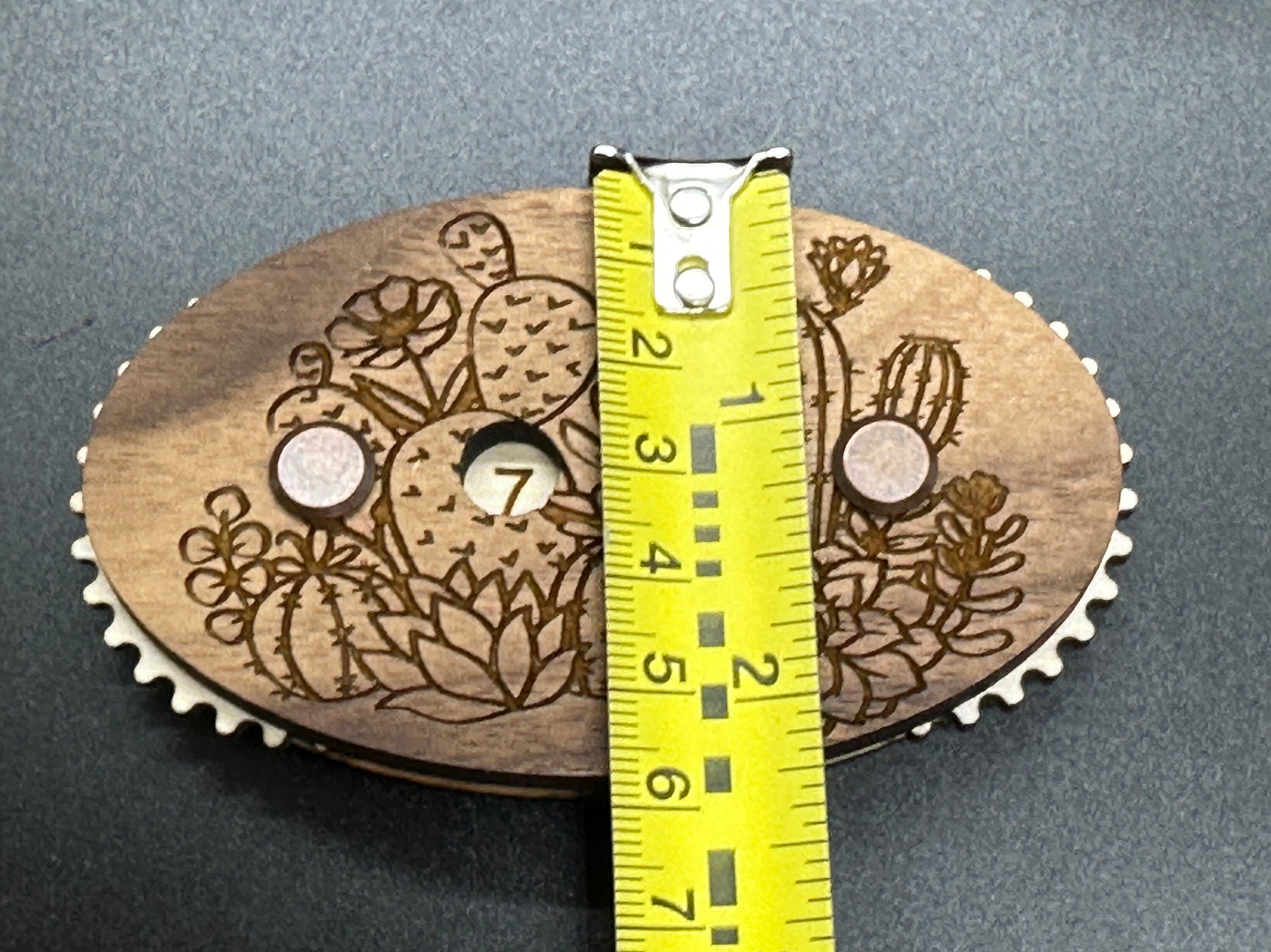 Wooden gear with laser-engraved design and a measuring tape for scale on a gray background