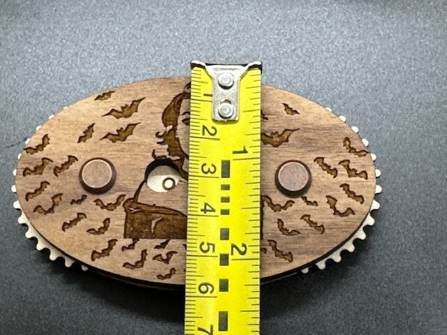Wooden gear with laser cut design and a measuring tape for scale on a gray background