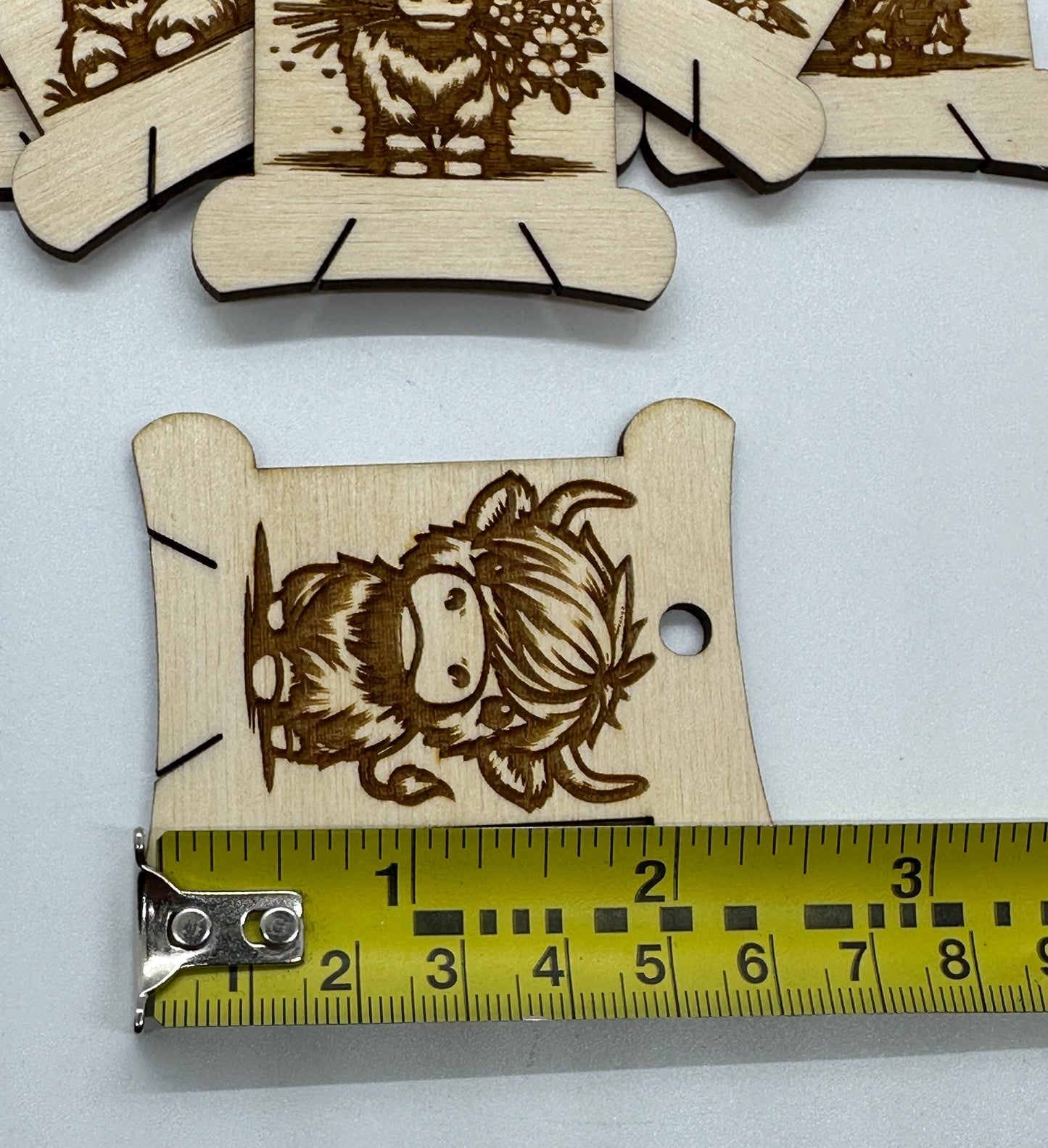 Wooden cutouts with laser-engraved designs on a white background, with a ruler for scale.