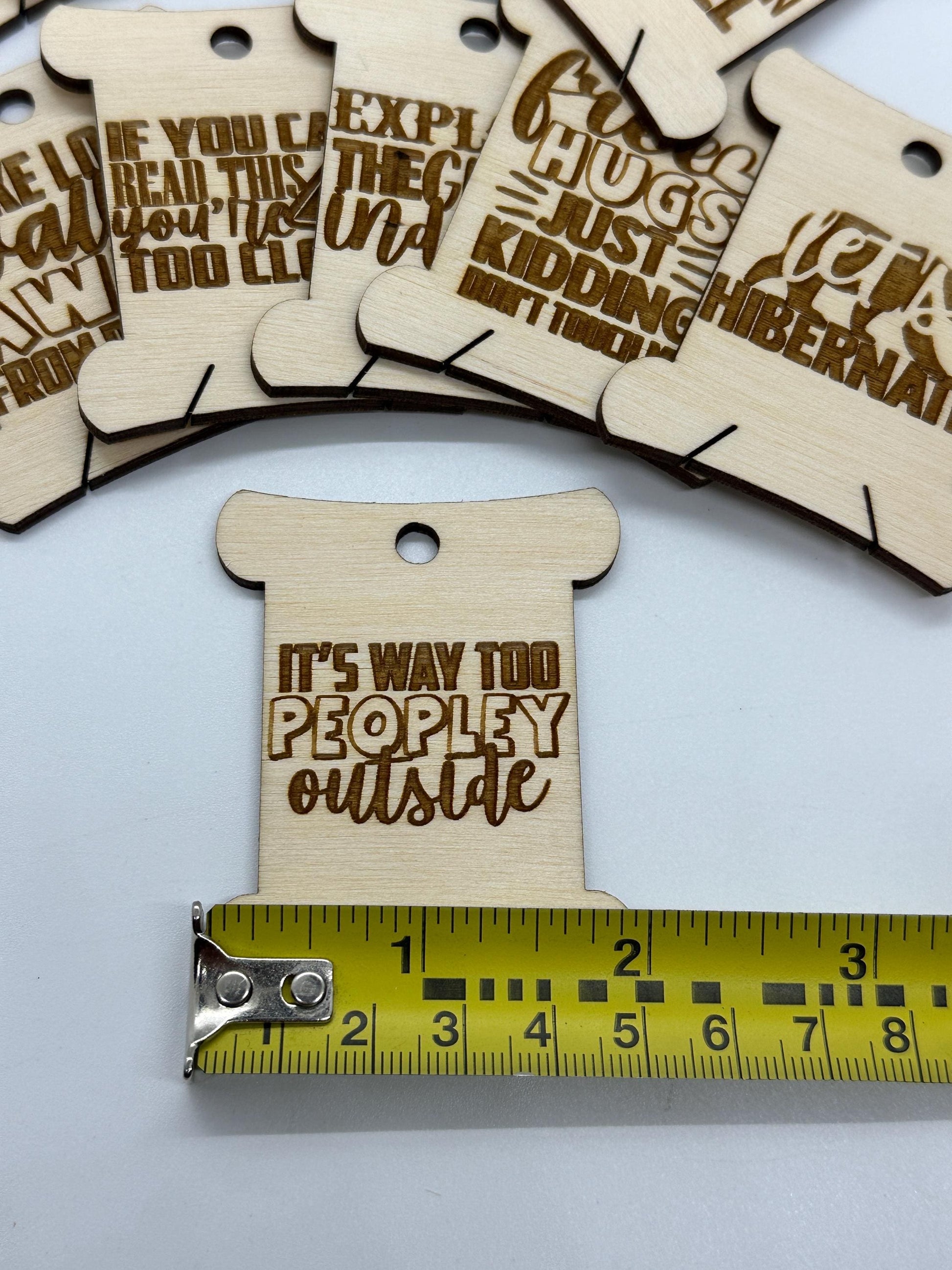 Wooden tags with engraved text on a white background with a measuring tape for scale.
