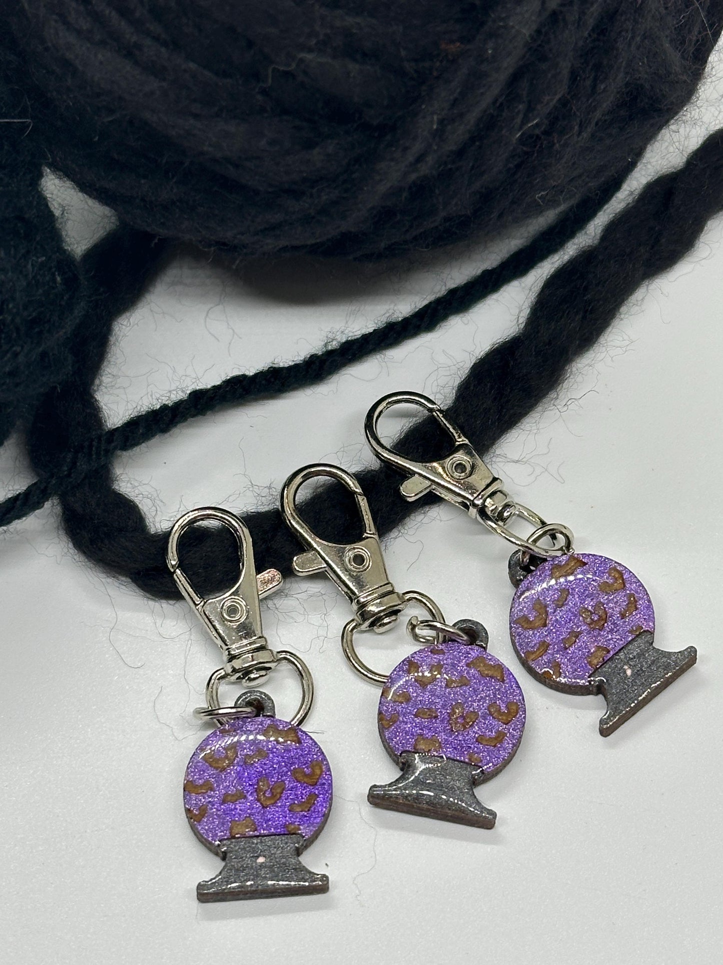 Purple and silver crystal ball keychain charms on a white surface with yarn in the background.