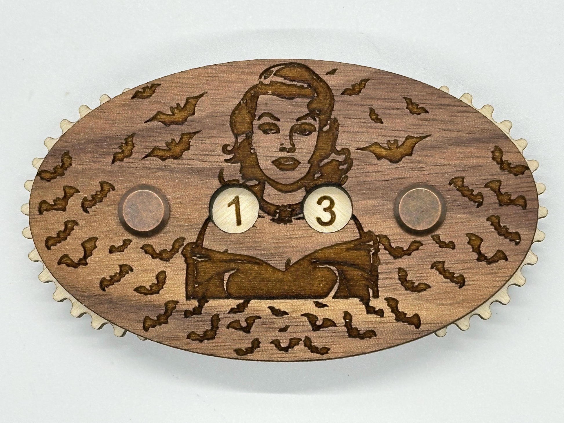 Wooden counter with engraved design of a woman and number 13, surrounded by bats on a white background.