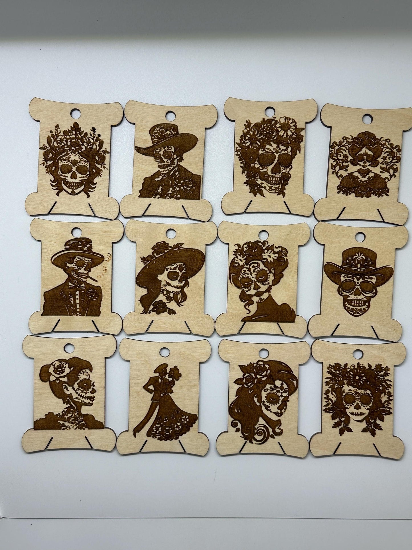 Nine wooden bobbins  with laser-cut decorative skull designs on a white background