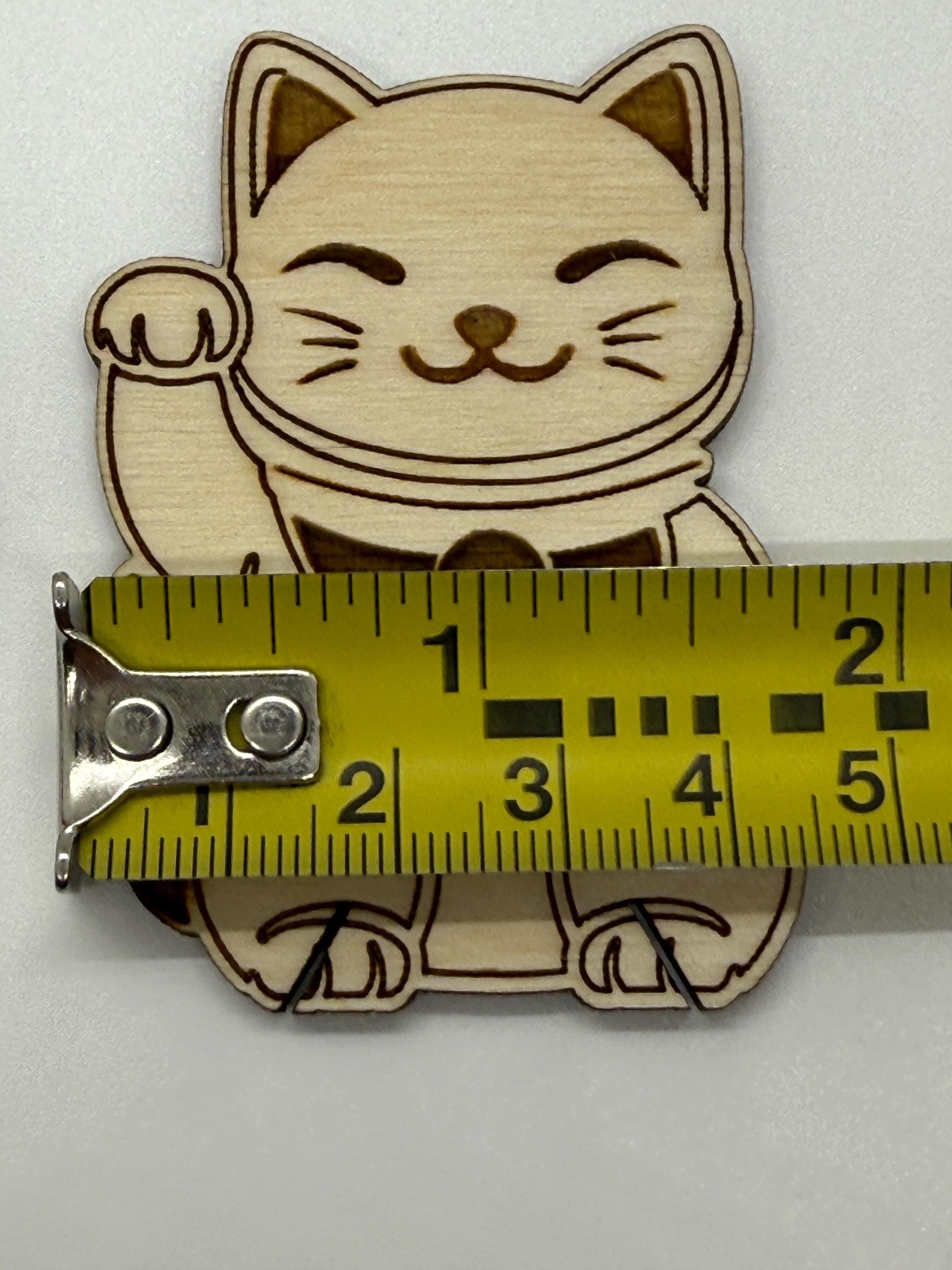 Wooden cat-shaped bobbin with a measuring tape for scale on a white background