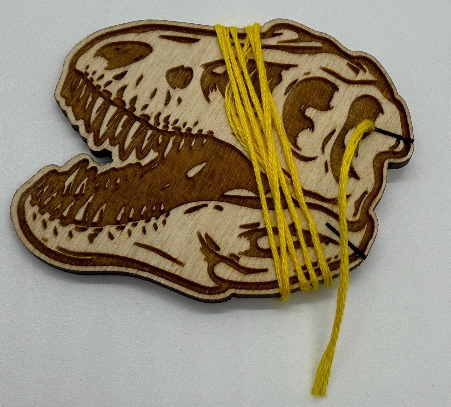 Set of 12 laser engraved dinosaur skull wooden bobbins on white background, detailed T-rex skull design on birch plywood