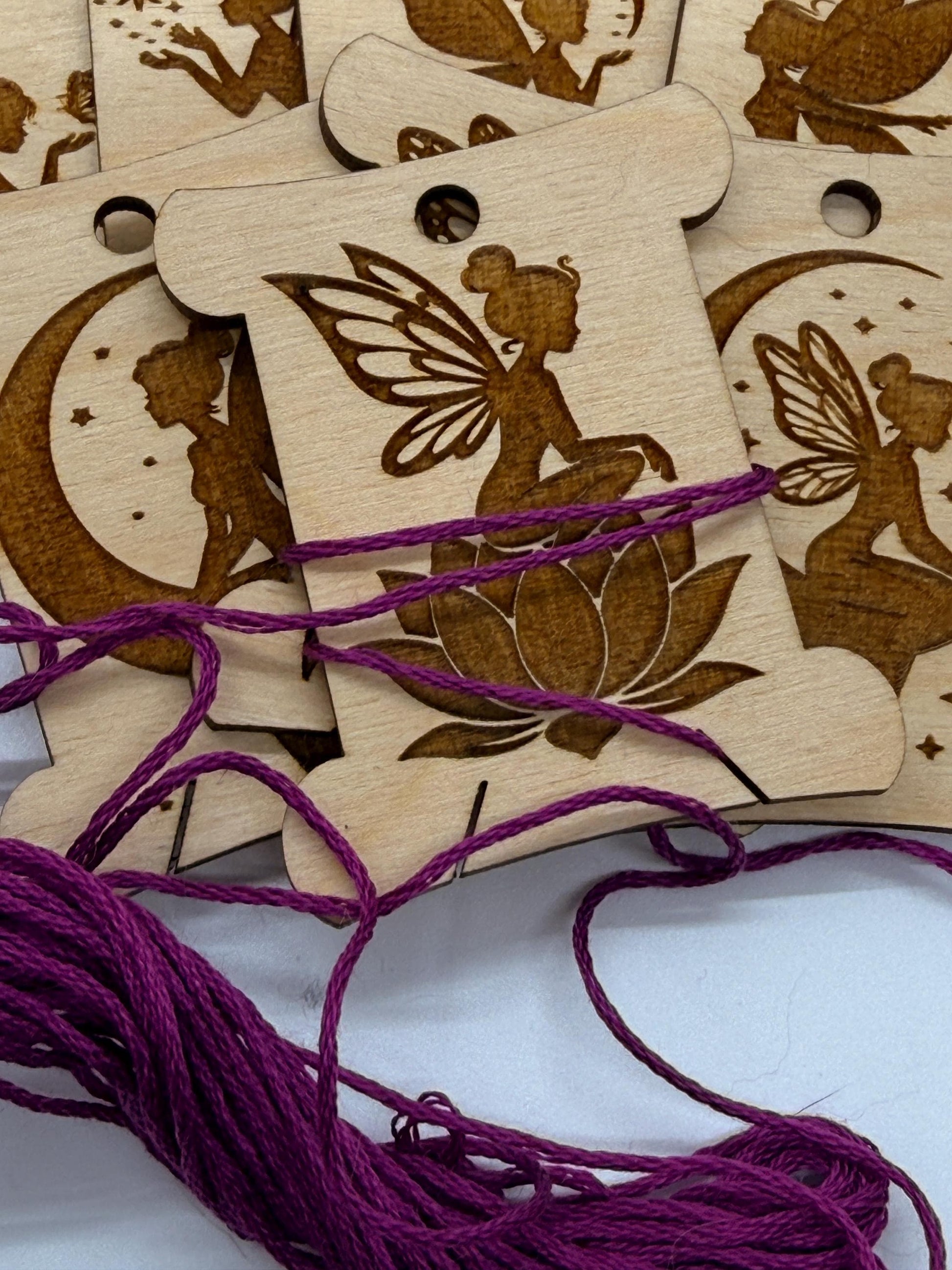 Wooden tags with fairy designs and purple string on a white background