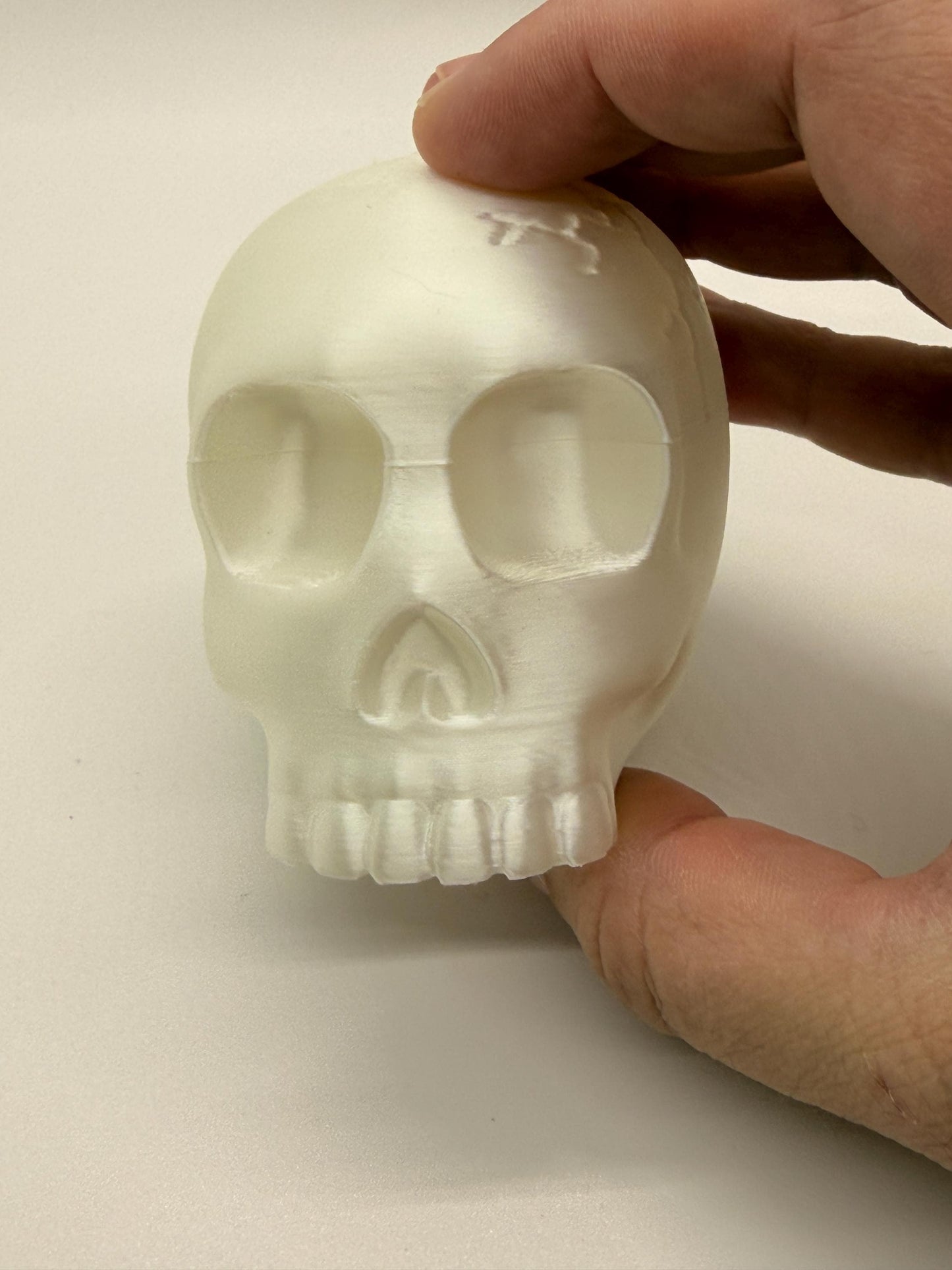 Skull-shaped object held by a hand on a plain background