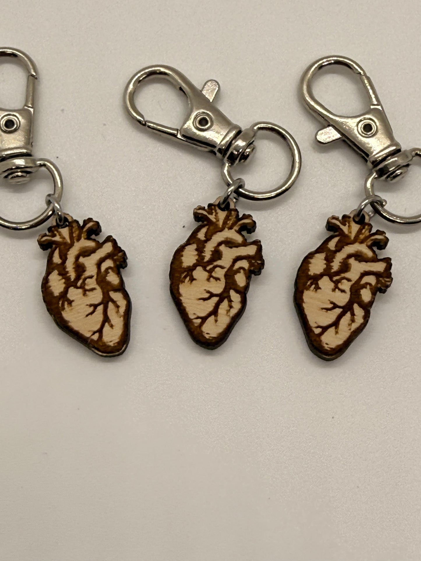 Three keychains with anatomical heart designs on a light gray background