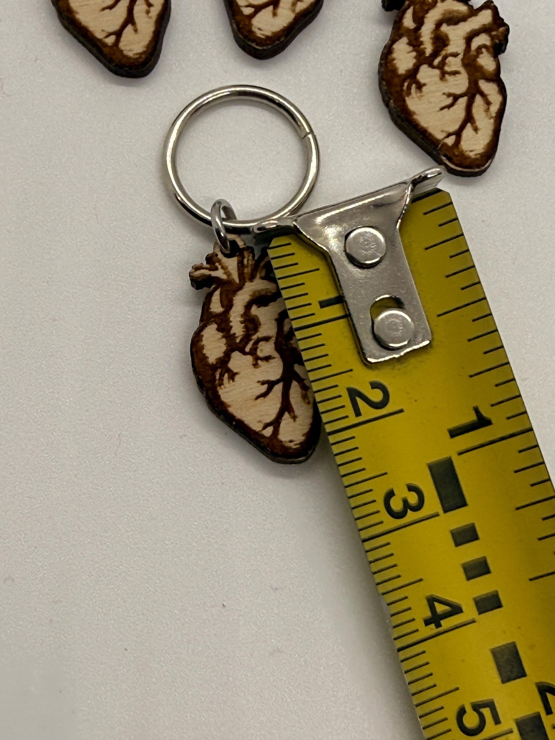 Keychain with anatomical heart design next to a measuring tape on a white background